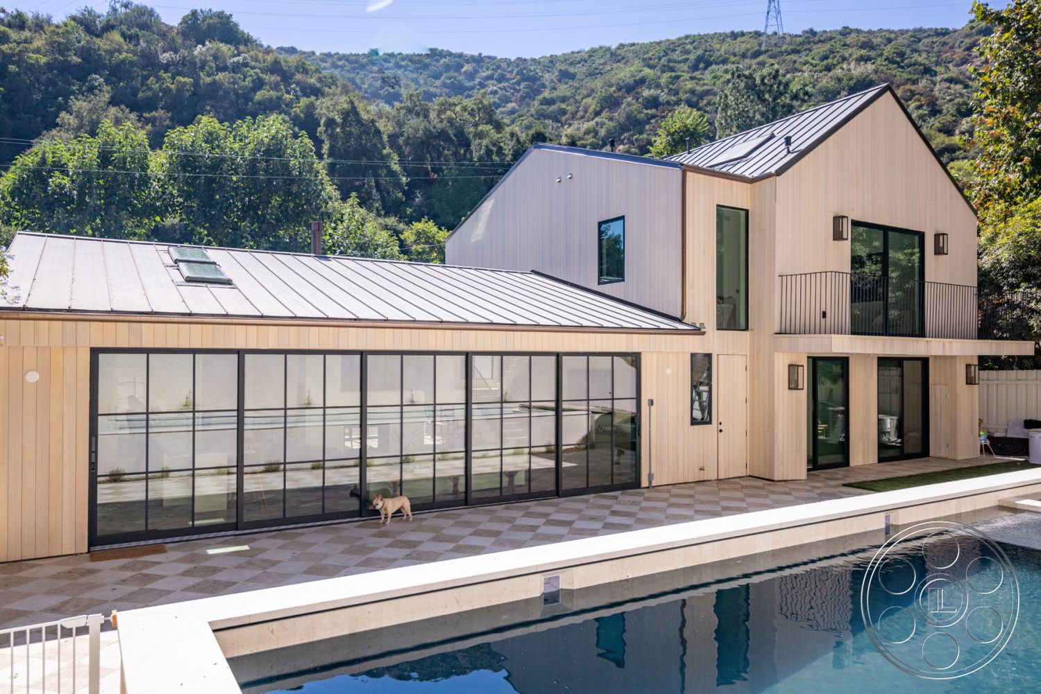 Modern Farmhouse 19 - large glass sliding doors, minimalist design elements, rectangular swimming pool, modern architectural style, floor-to-ceiling glass windows, interior glass wall partition, concrete pool coping, wood siding exterior, natural hillside setting, exposed steel frame, vaulted ceilings, metal standing seam roof, planked wood deck, chequered stone patio flooring, horizontal wood railing, landscape greenery backdrop