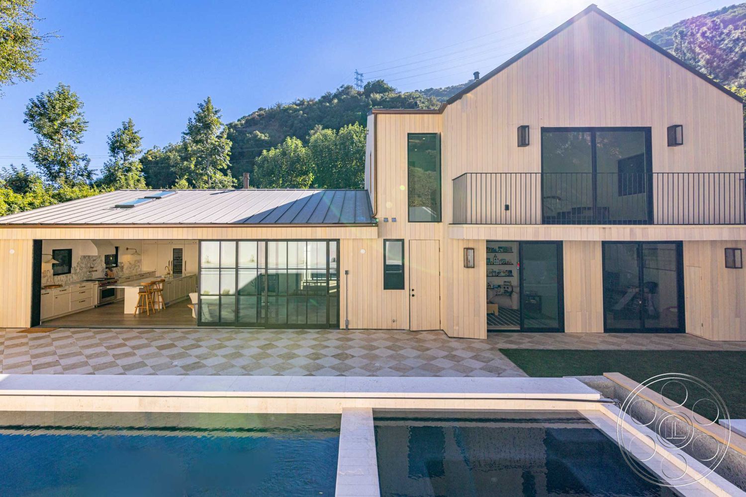 Modern Farmhouse 19 - glass sliding doors, rectangular swimming pool, floor-to-ceiling windows, outdoor dining area, modern architectural style, concrete pool deck, minimalist outdoor space, exposed wood ceiling beams, landscaped garden area, open concept kitchen layout, natural light-filled interior, metal roof panels, exterior wooden siding, mountain backdrop view, chiseled stone pool coping, checkerboard stone patio flooring, softened geometric shapes, balcony with black metal railing, sliding glass partitions, wooden kitchen cabinetry