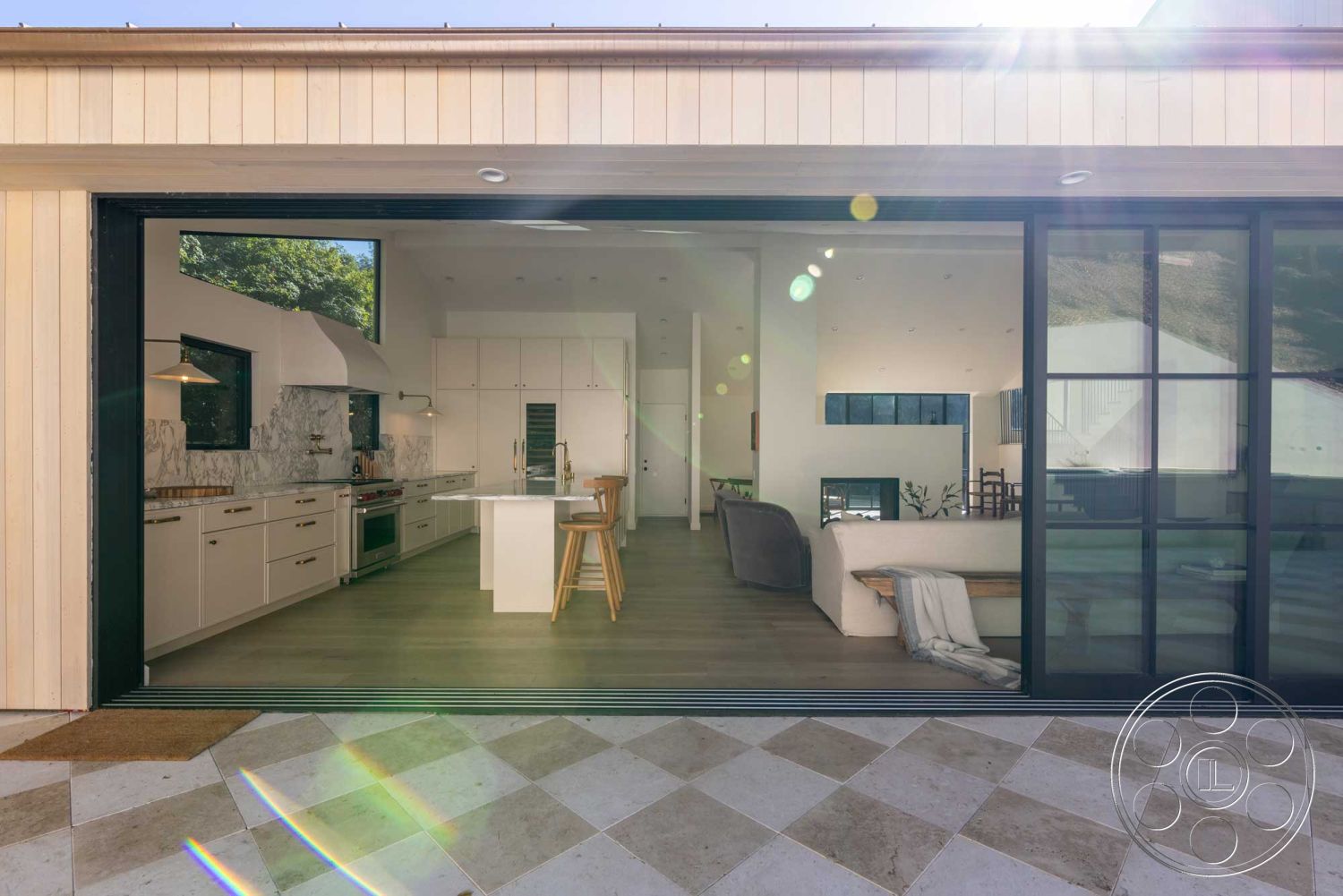 Modern Farmhouse 19 - exterior, stone accent wall, stainless steel appliances, glass sliding doors, open-concept living space, concrete patio flooring, rectangular kitchen island, textured ceiling details, modern minimalist design, wood beam ceiling, marble kitchen backsplash, hardwood kitchen floors, white painted walls, vaulted living room ceiling, natural light abundance, urban hillside setting, black-framed windows, curved outdoor seating area