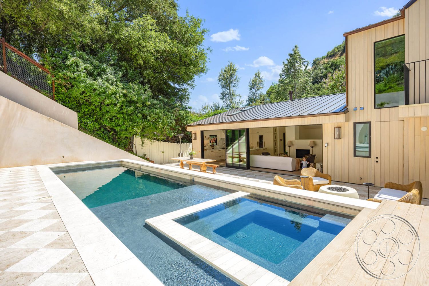 Modern Farmhouse 19 - exterior, large glass windows, sliding glass doors, modern outdoor furniture, concrete pool deck, metal roof, open-concept living area, exposed aggregate concrete wall, rectangular infinity pool, natural light-filled interior, surrounding hillside view, wood siding exterior, landscaped hillside garden, travertine tile patio flooring, wooden outdoor lounge area