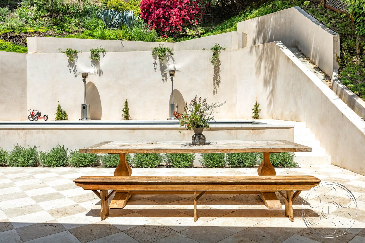 Modern Farmhouse 19 - exterior, outdoor entertaining space, raised garden beds, natural wood bench, minimalist outdoor decor, architectural landscaping, sun-drenched patio, minimalist garden design, modern outdoor living area, rectangular outdoor dining table, secluded backyard setting, smooth stucco walls, textured stone patio flooring, curved stone steps, step-up stone terrace, landscaped greenery with flowering plants, water feature with fountain, Mediterranean-inspired design