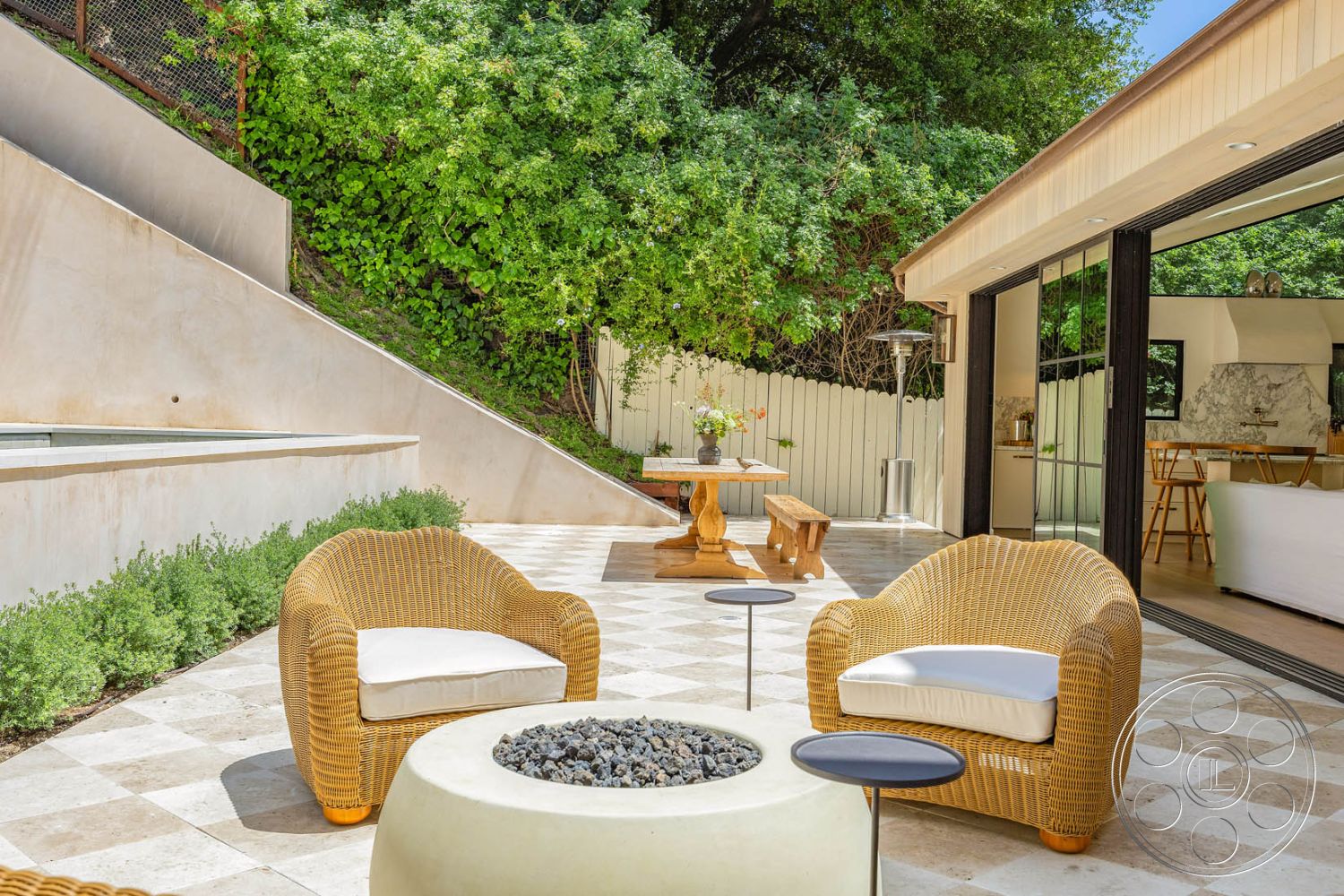 Modern Farmhouse 19 - concrete retaining wall, shaded outdoor seating area, textured plaster wall finish, exterior patio flooring, modern outdoor space with minimalist design, rectangular wooden dining table, multi-level outdoor space, curved patio edge, wicker outdoor seating, stone tile patio flooring, circular fire pit with lava stones, landscaped green hillside backdrop, wall-mounted patio heater, sliding glass door entryway, natural light-filled area with greenery, high wooden fence for privacy