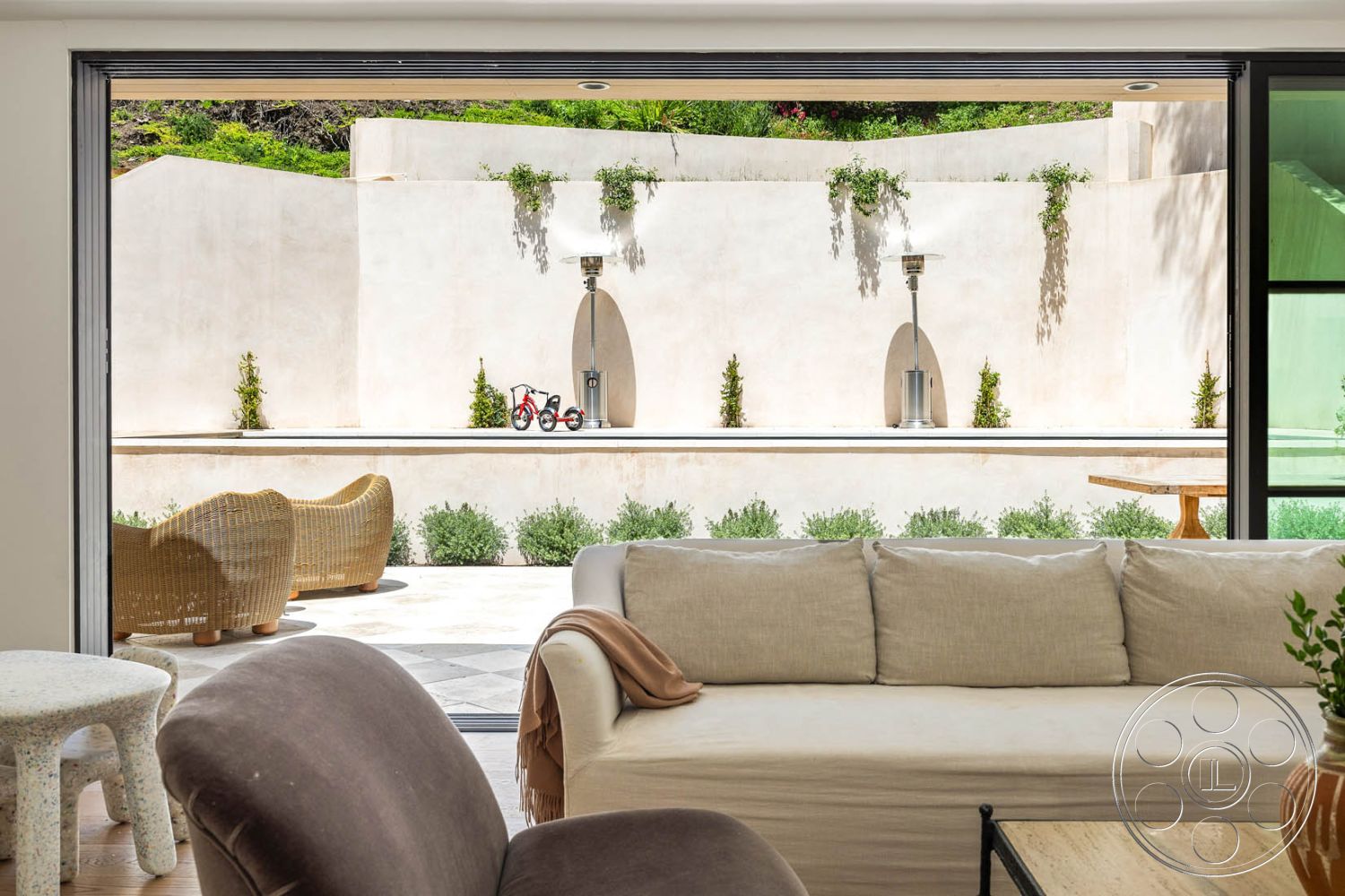 Modern Farmhouse 19 - contemporary design elements, interior living room with linen sofa, exterior courtyard with smooth plaster walls, exterior concrete patio with modern furniture, exterior rectangular pool with water features, natural stone flooring in patio area, steel and glass sliding doors, wooden table in outdoor dining space, lush greenery in courtyard setting, textured concrete wall with plants, outdoor seating with woven chairs, interior design featuring minimalistic decor, large glass windows providing natural light, urban residential setting with greenery