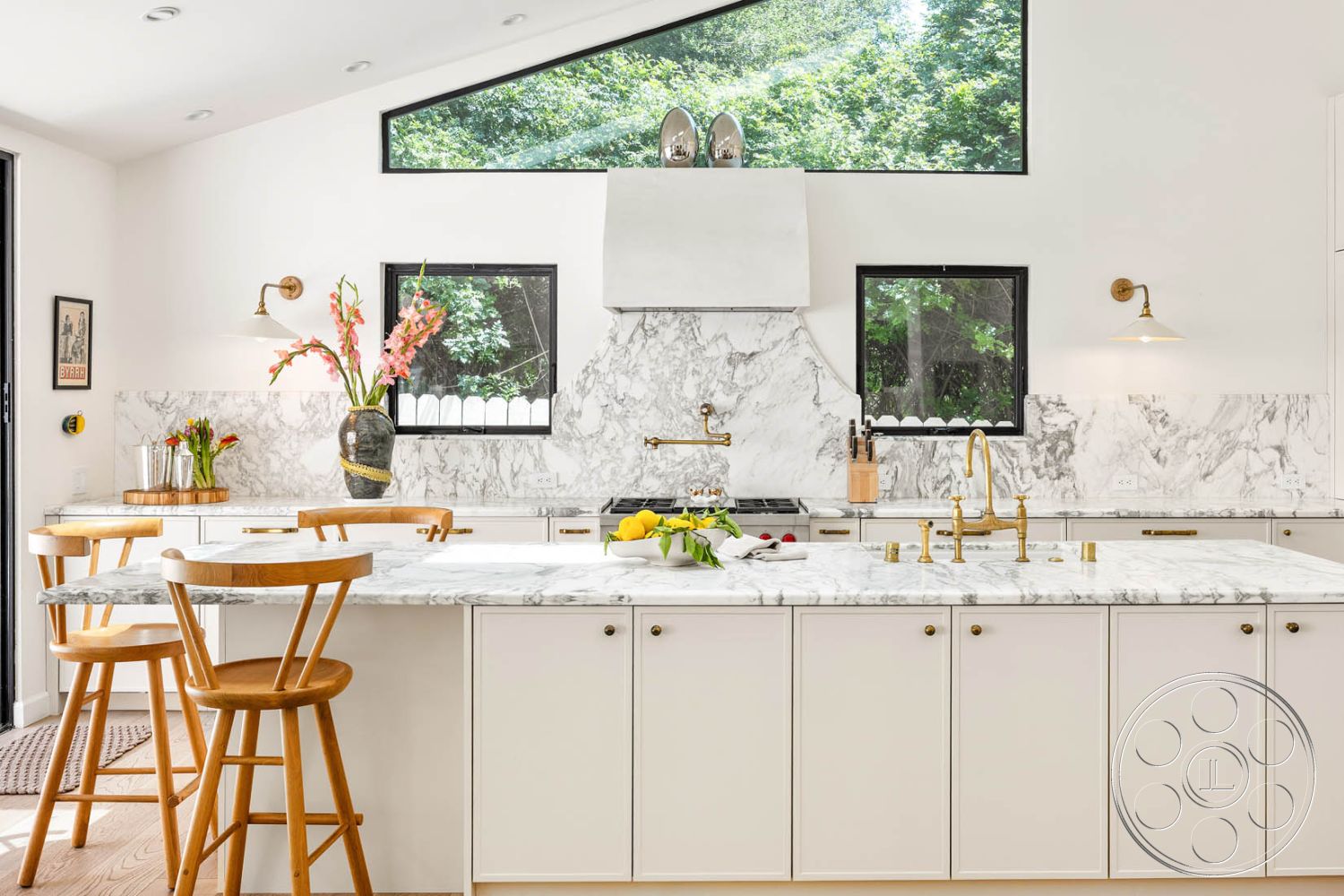 Modern Farmhouse 19 - wooden bar stools, stainless steel appliances, white marble backsplash, interior kitchen with marble countertops, natural light-filled space, marble kitchen island, large black-framed windows, white cabinetry with gold hardware, minimalist kitchen style, open concept kitchen design, suburban kitchen setting, wood flooring in kitchen, light fixture with gold accents