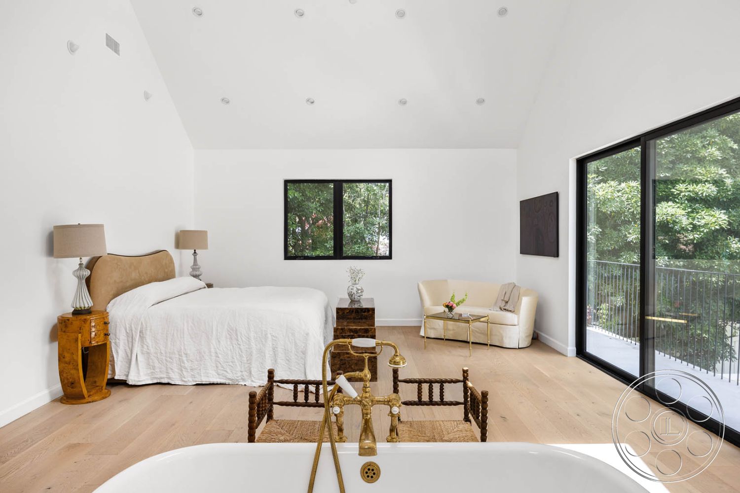 Modern Farmhouse 19 - natural light interior, hardwood bedroom floors interior, neutral color palette interior, white painted walls interior, floor-to-ceiling windows interior, minimalist decor interior, vaulted ceiling interior, modern bed frame interior, golden brass faucet interior, decorative side table interior, soft armchair interior, landscaped view exterior, modern wall art interior, window balcony exterior