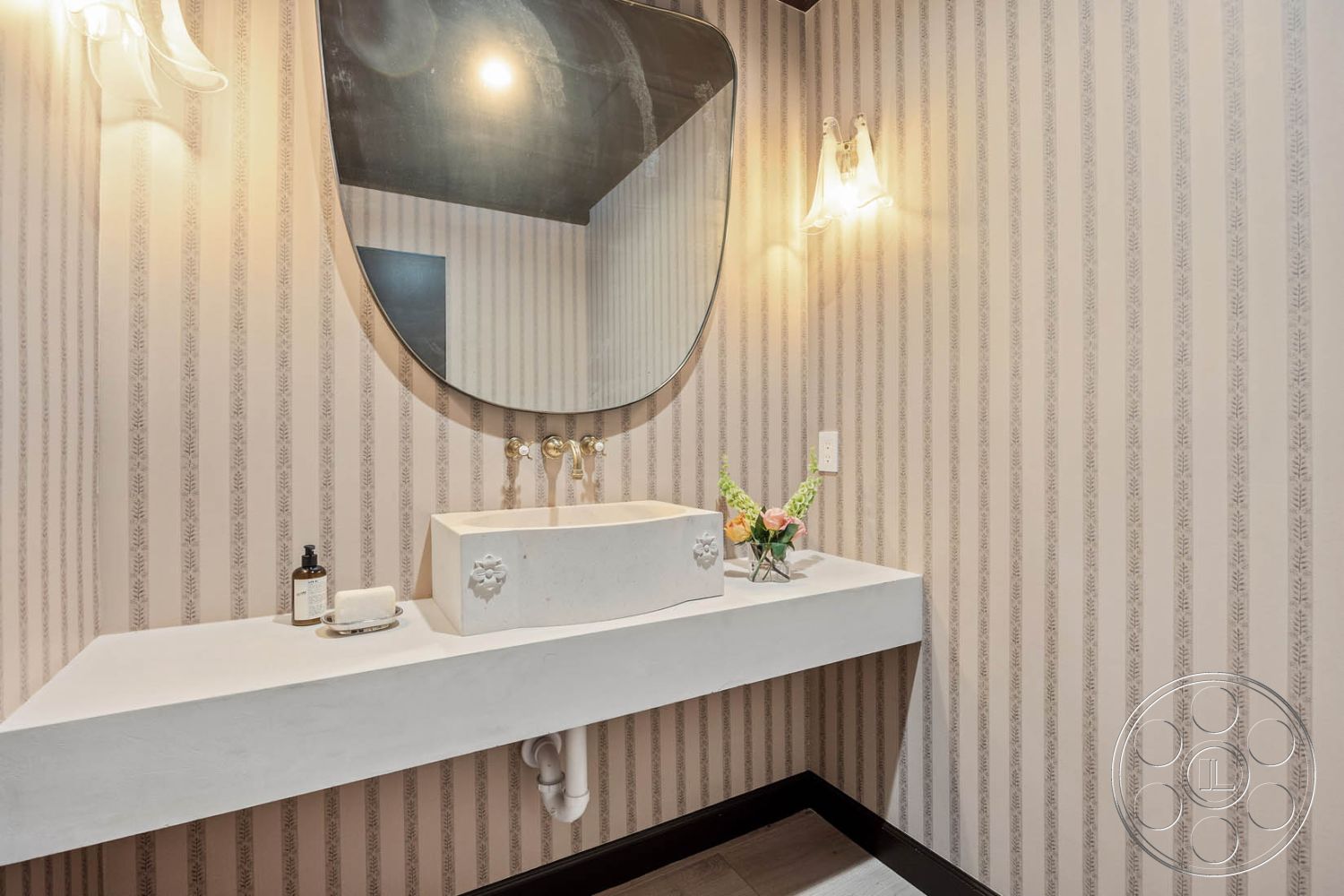 Modern Farmhouse 19 - polished tile flooring, white porcelain sink, minimalist bathroom design, modern bathroom interior, concrete floating vanity countertop, oval mirror above sink, striped wallpaper interior, wall-mounted sconces lighting, dark wood accent trims, vanity area with decorative flowers