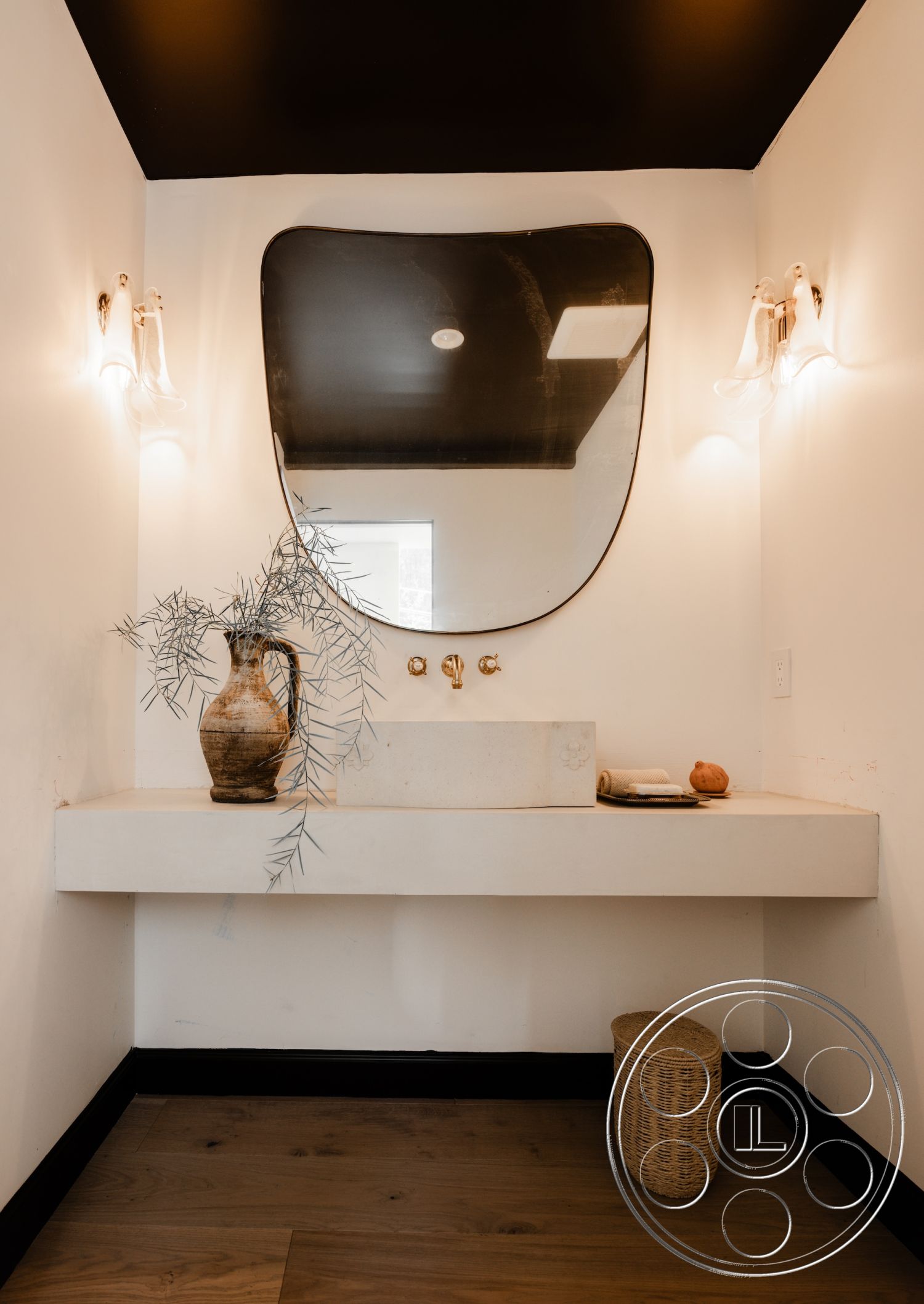 Modern Farmhouse 19 - minimalist decor, black ceiling, curved mirror, gold faucet fixtures, interior bathroom, wooden floorboards, concrete sink countertop, smooth white plaster walls, ambient wall sconces, natural vase arrangement