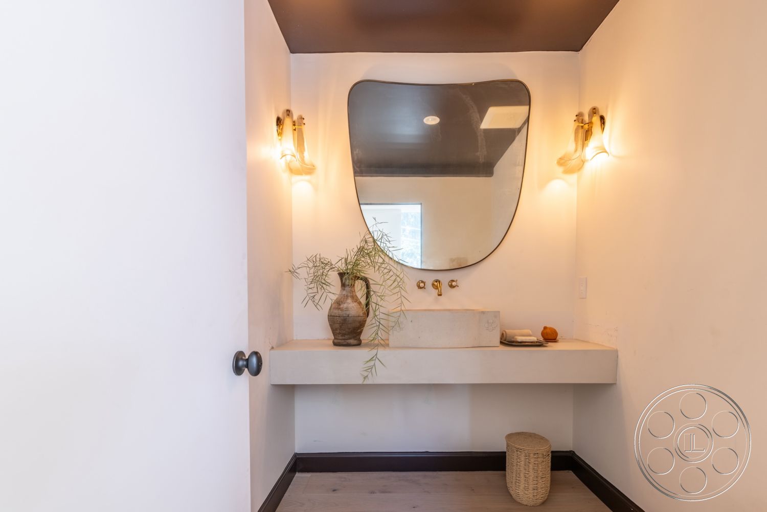 Modern Farmhouse 19 - gold faucet fixtures, interior bathroom design, textured ceiling with dark paint, exposed concrete bathroom sink countertop, oval mirror with organic shape, modern sconce lights, minimalist wall treatment with white painted walls, dark wood floor in bathroom, natural decor with potted plants