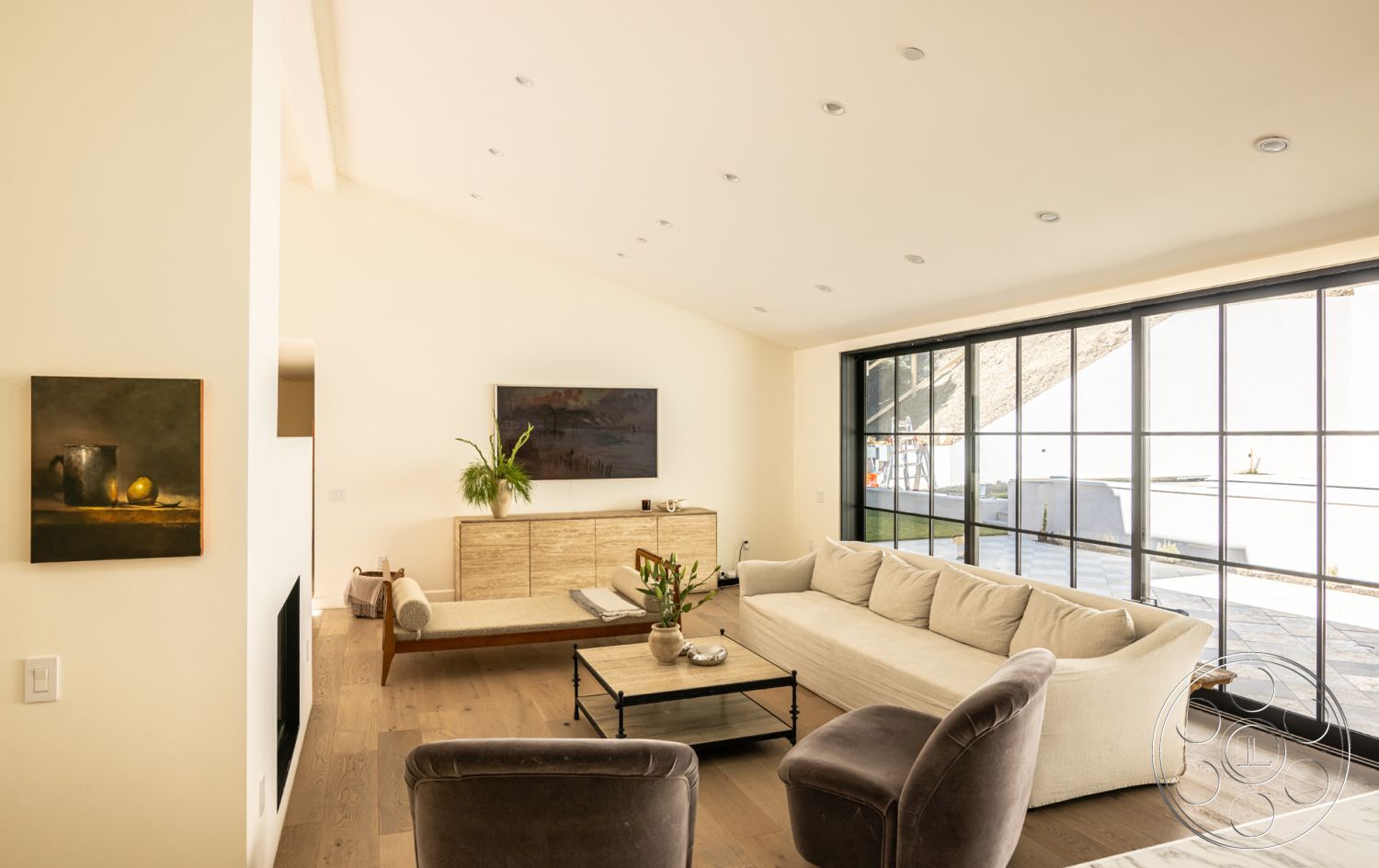 Modern Farmhouse 19 - neutral color palette, natural light, decorative art piece, open floor plan, textured wall finish, light wood cabinetry, floor-to-ceiling windows, vaulted ceiling, minimalist coffee table, greenery accent, contemporary living room, black metal window frames, hardwood living room floors, modern sectional sofa