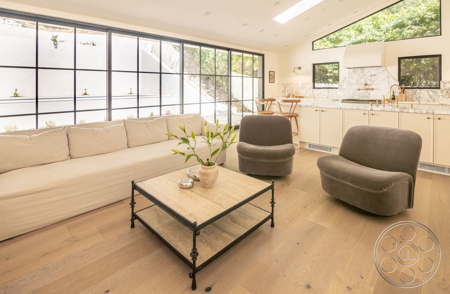 Modern Farmhouse 19 - interior hardwood living room floors, interior marble kitchen countertop, interior open concept living space, interior recessed lighting details, interior contemporary design style, interior beige fabric sectional sofa, interior black metal framed windows, interior light wood dining chairs, interior minimalist coffee table with stone top, interior wall with white painted finish, interior potted plant décor, interior modern gray lounge chairs, interior vaulted ceiling design, interior natural light abundant