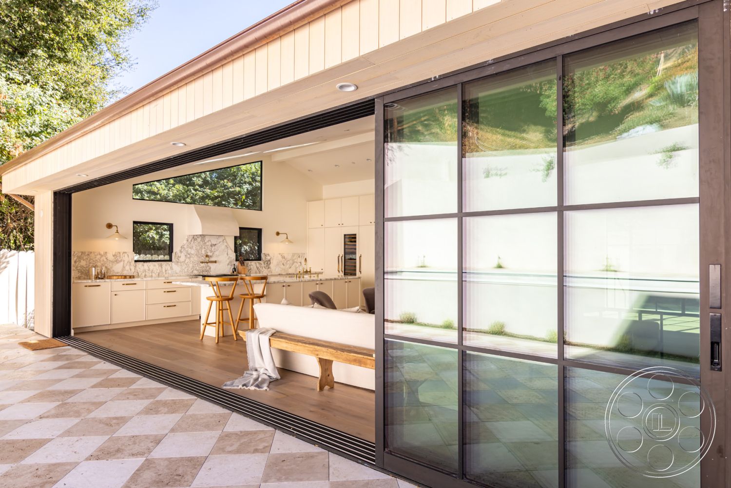 Modern Farmhouse 19 - landscaped garden view, wooden ceiling beams, open-concept living space, large floor-to-ceiling windows, stainless steel kitchen appliances, interior kitchen with marble countertops, exterior sliding glass doors, exposed brick accent wall, hardwood flooring in living area, comfortable outdoor seating, natural light-filled interior, contemporary outdoor setting, subway tile kitchen backsplash, modern minimalist architectural style, rectangular outdoor patio, farmhouse-style kitchen cabinets, checkerboard tile flooring in patio area, urban backyard space, pivoting glass door access, tiled pool area adjacent to patio