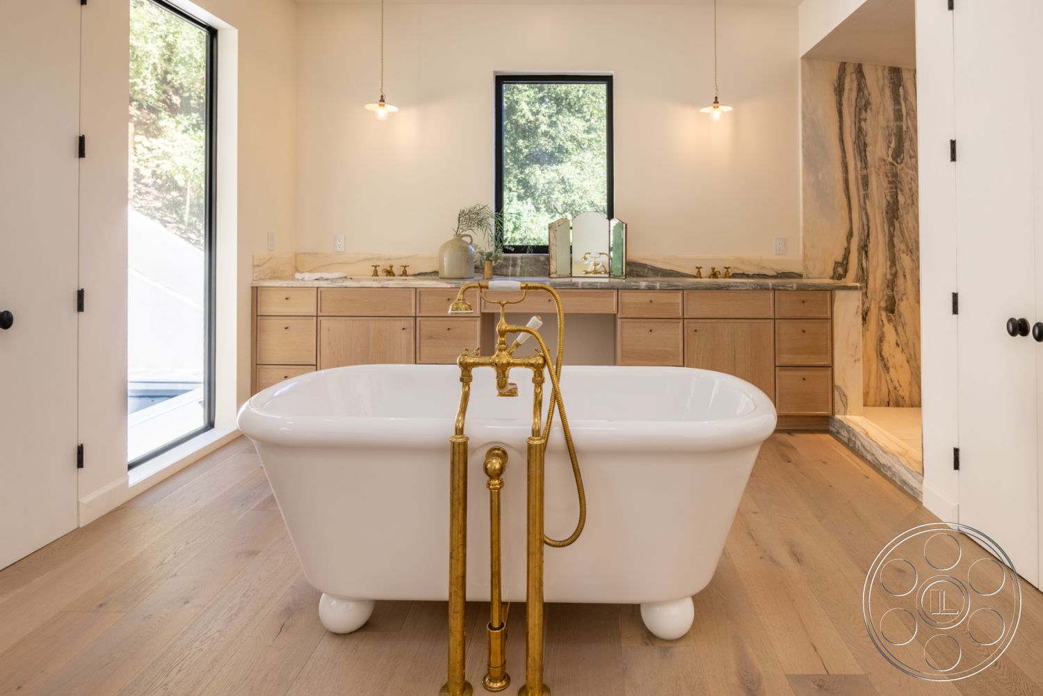 Modern Farmhouse 19 - light hardwood flooring, spa-like atmosphere, modern aesthetic, contemporary design elements, textured plaster walls, large black framed windows, marble countertop with veining, minimalist pendant lighting, interior bathroom, freestanding white bathtub, natural setting view, golden floor-mounted bathtub faucet, natural wood cabinet storage