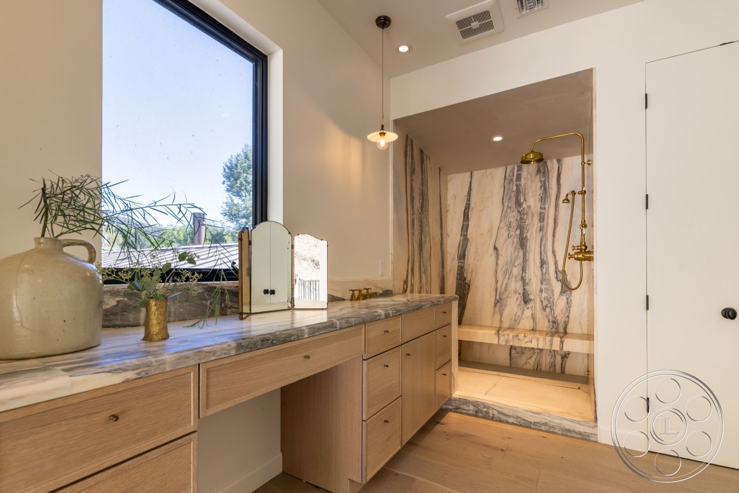 Modern Farmhouse 19 - neutral color palette, decorative plants, modern lighting fixtures, textured plaster walls, exposed wood flooring, interior bathroom, minimalist bathroom decor, marble shower walls, golden faucet fixtures, marble shower floor, wood vanity with drawers, large black-framed window, built-in shower bench