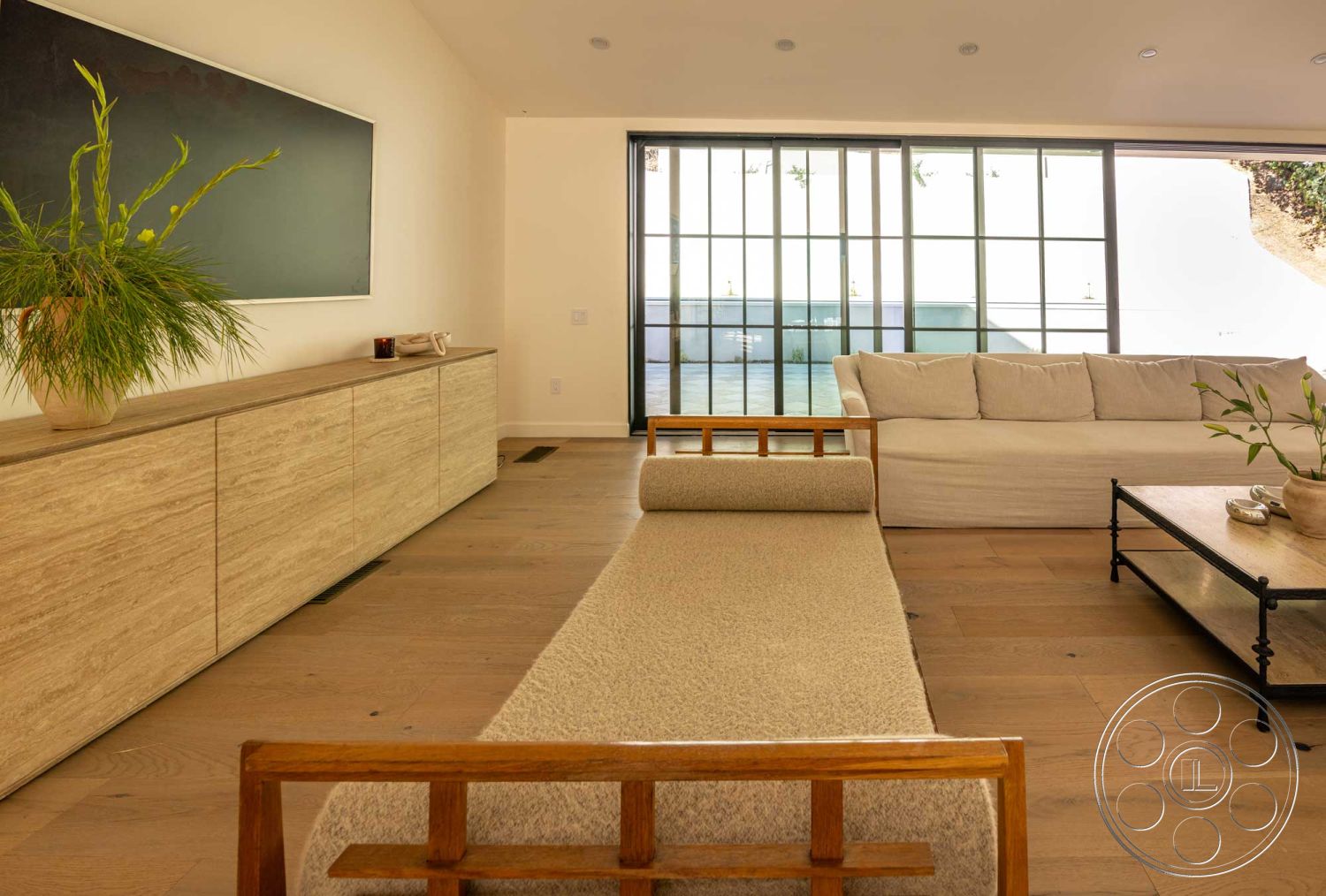 Modern Farmhouse 19 - textured area rug, wooden sideboard, single-story home, hardwood living room floors, modern minimalist design, open floor plan layout, neutral painted walls, floor-to-ceiling glass windows, indoor plant accent, natural light-filled room, interior living area, contemporary home decor, sand-colored fabric sofa, minimalist wooden coffee table, exposed wooden furniture