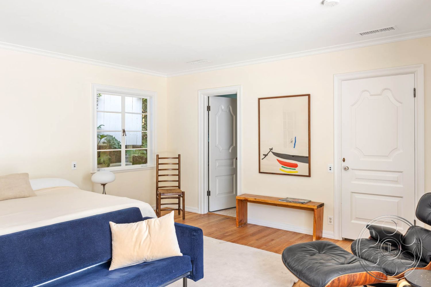 English 60 - textured area rug, modern art wall decor, mid-century modern furniture, hardwood bedroom floors, cream painted walls, open bedroom layout, exposed white ceiling, rectangular wooden bench, chrome desk lamp, plush throw pillow, windows with white trim, double doors with decorative panels