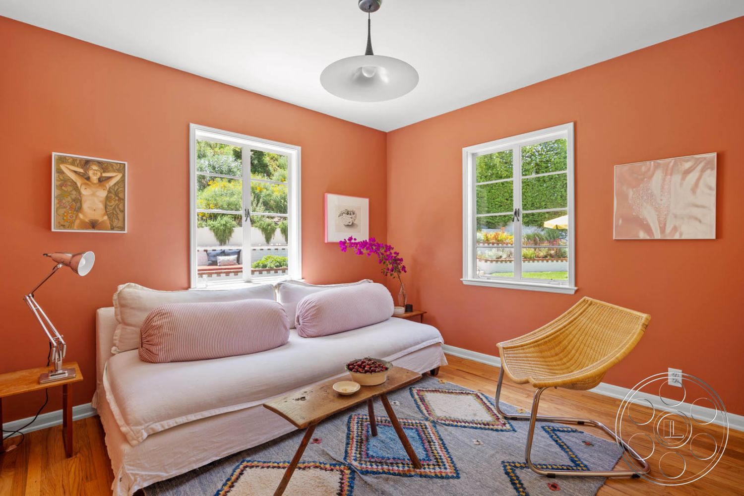 English 60 - hardwood flooring, textured area rug, woven chair, decorative wall art, metal desk lamp, wooden side table, casual living space, cozy sitting area, minimalist design aesthetic, large windows with white trim, orange painted walls, stylish sofa with striped cushions, greenery view from windows