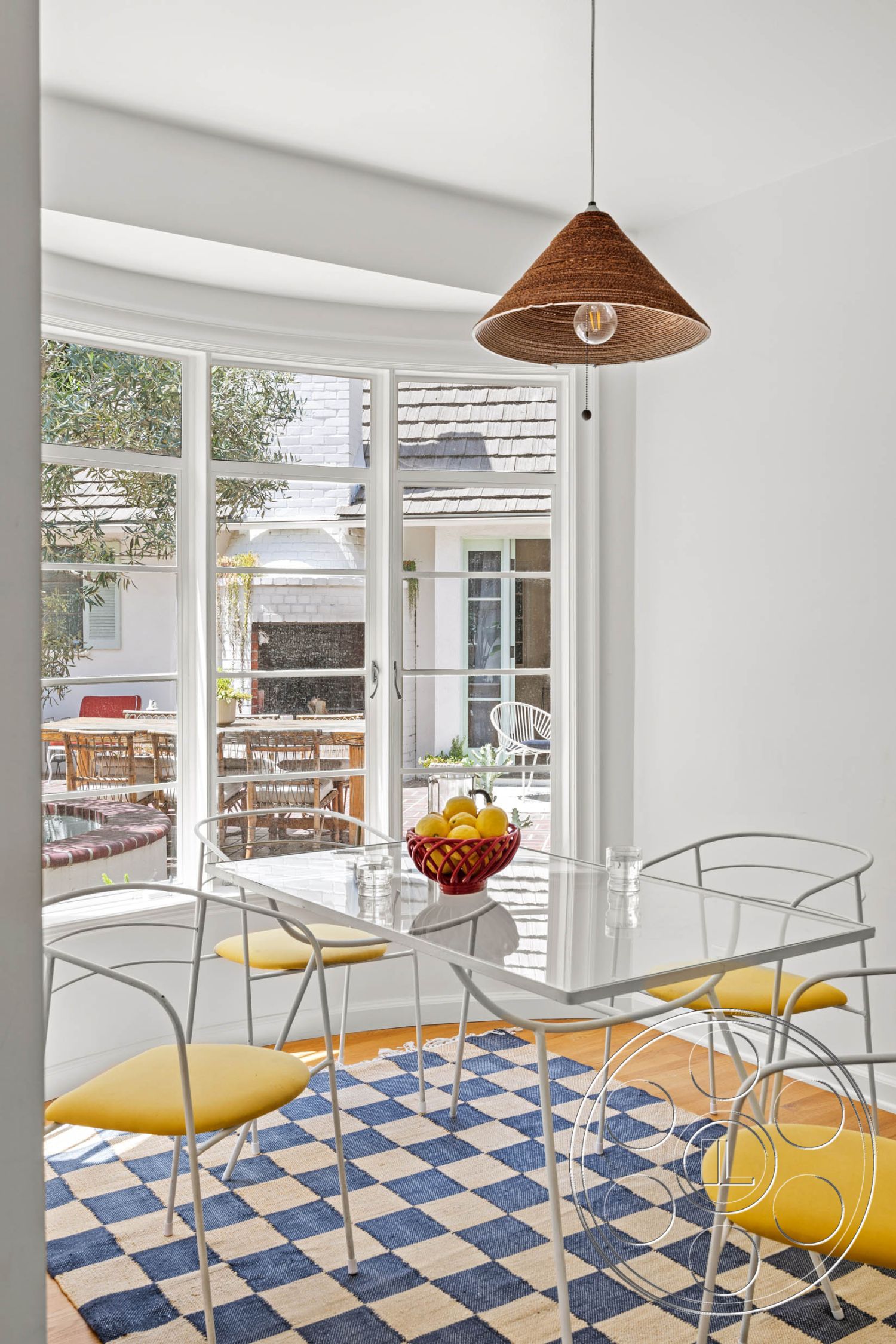 English 60 - natural light, contemporary style, hardwood flooring, modern design, open floor plan, indoor-outdoor flow, glass dining table, metal dining chairs, interior dining area, woven pendant light fixture, white painted walls, curved bay window, view of outdoor patio, yellow upholstered chairs, checkerboard area rug