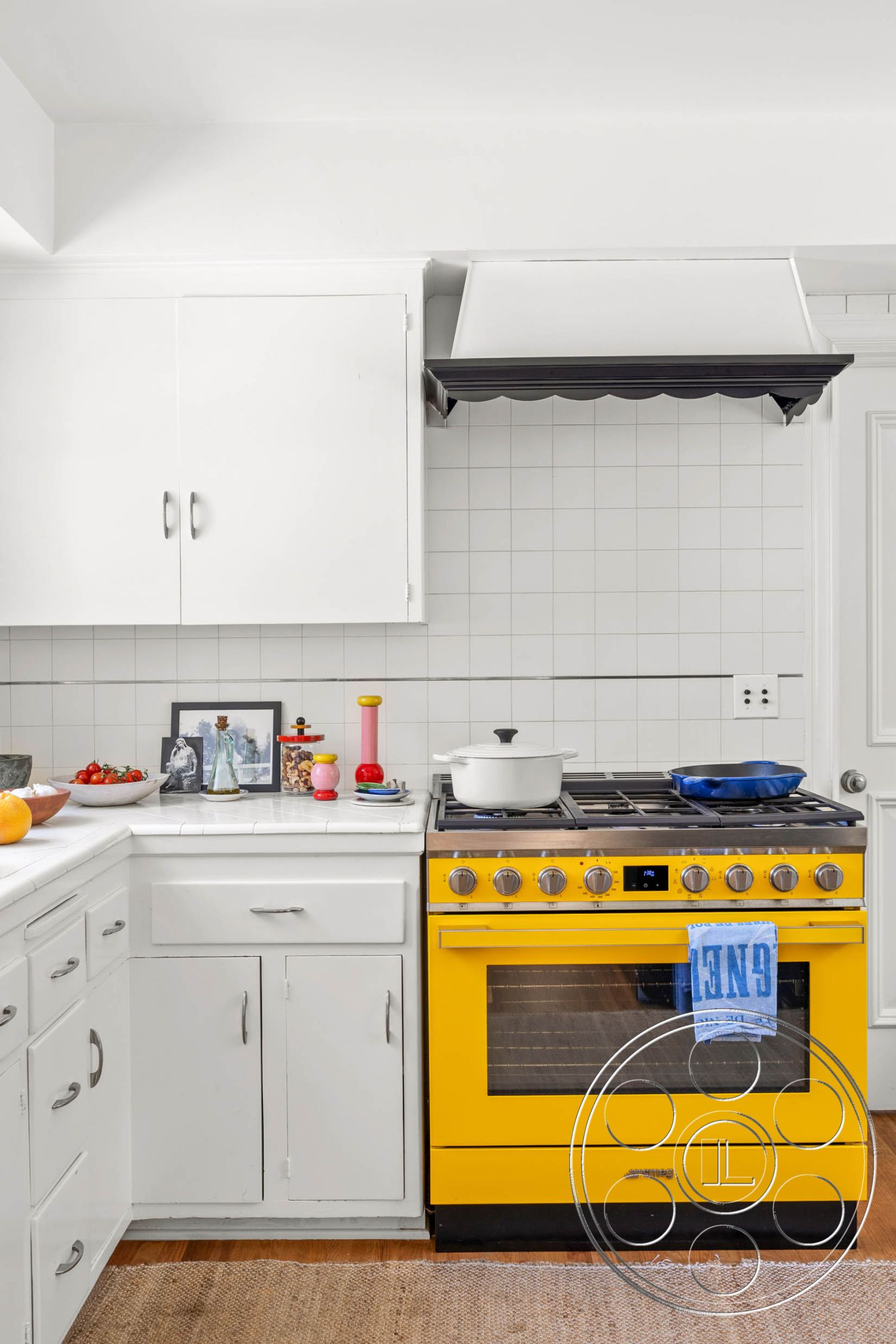 English 60 - stainless steel kitchen appliances, interior kitchen space, minimalist kitchen design, hardwood kitchen flooring, exposed wood trim details, white cabinetry kitchen storage, subway tile backsplash kitchen, gas range with yellow finish, countertop with decorative items, rectangular kitchen layout