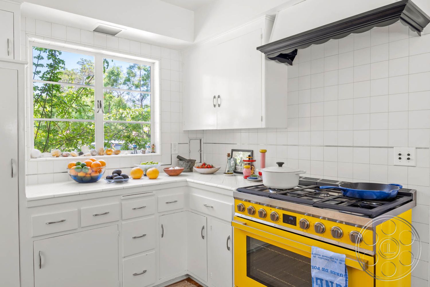 English 60 - minimalist decor, natural light, wood flooring, functional workspace, contemporary design elements, fruit bowl centerpiece, modern kitchen design, open kitchen layout, interior kitchen, built-in kitchen cabinets, white painted cabinetry, stainless steel countertop, white tiled backsplash, yellow gas range stove, corner window with green view