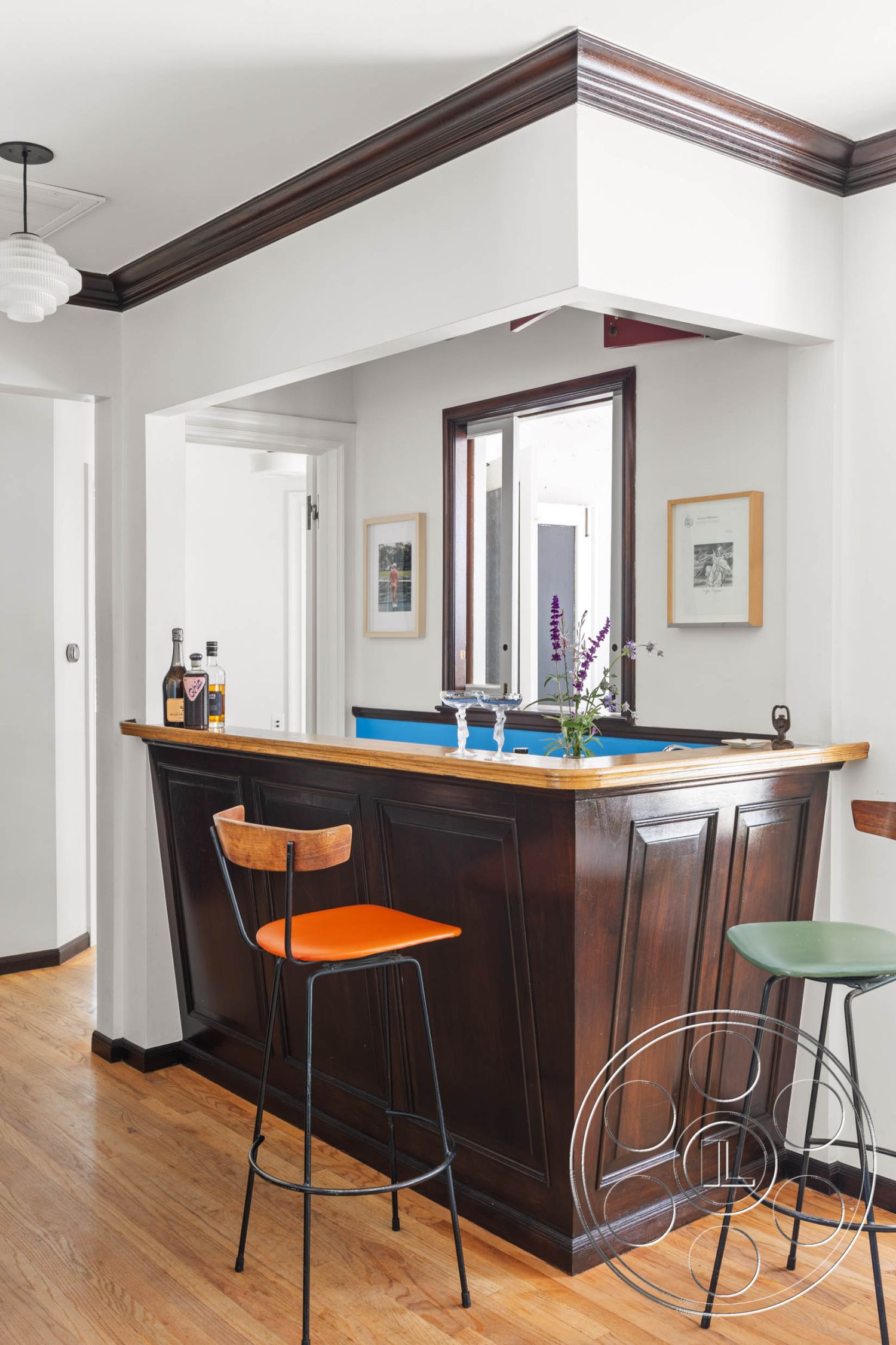 English 60 - light hardwood flooring, contemporary design elements, white painted walls, minimalist interior style, exposed wood crown molding, open floor plan with natural light, framed artwork wall decor, interior bar with wood paneling, dark wood bar countertop, modern bar stools with colored seats, large window with sliding doors, geometric bar shape