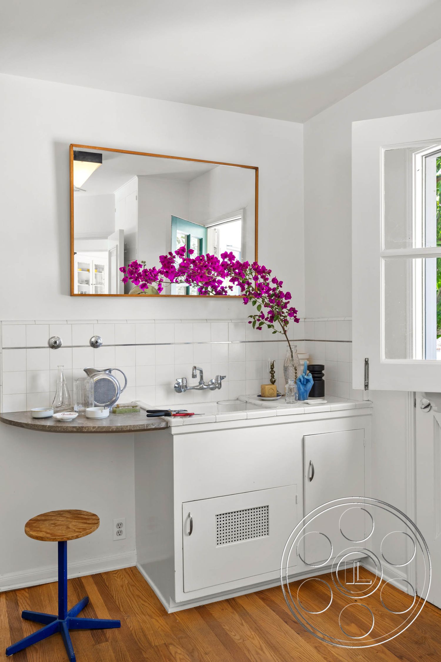 English 60 - marble countertop, hardwood floor, natural light from windows, modern minimalist style, white painted walls, interior kitchen area, framed wall mirror, decorative flower arrangement, white tile backsplash, round wooden stool, metal base stool