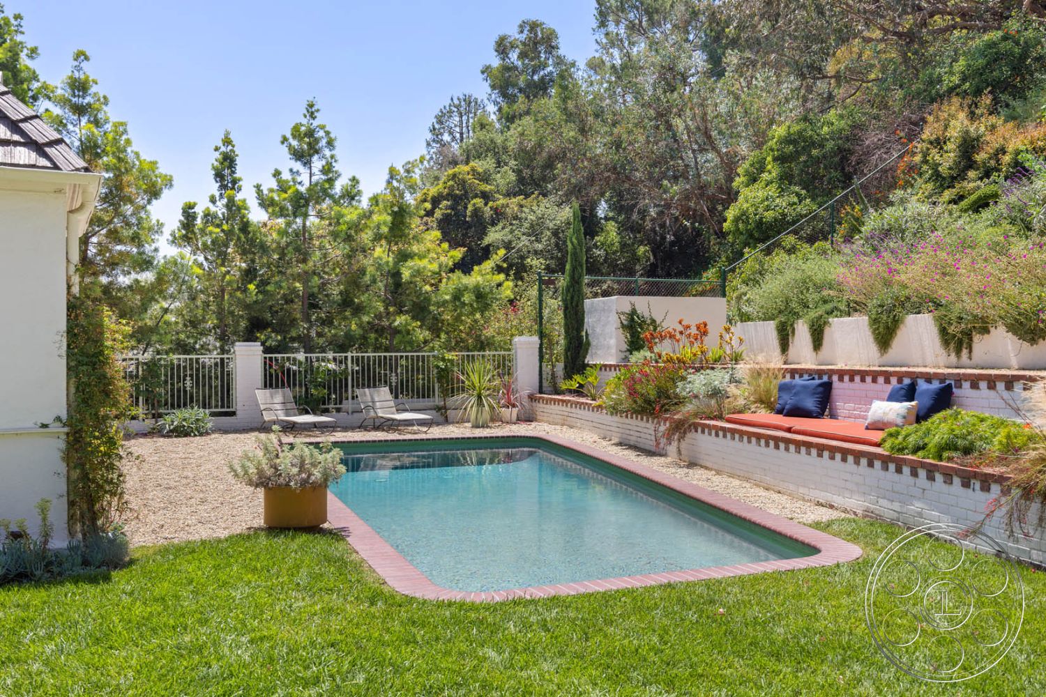 English 60 - rectangular swimming pool, grassy lawn, privacy fence, exterior concrete pool border, brick patio edging, sunny outdoor environment, landscaped garden with native plants, tropical garden setting, patio area with lounge chairs, multi-level outdoor seating, brick seating wall, concrete wall with planter beds, ceramic outdoor cushions, smooth gravel ground covering, backyard relaxation area