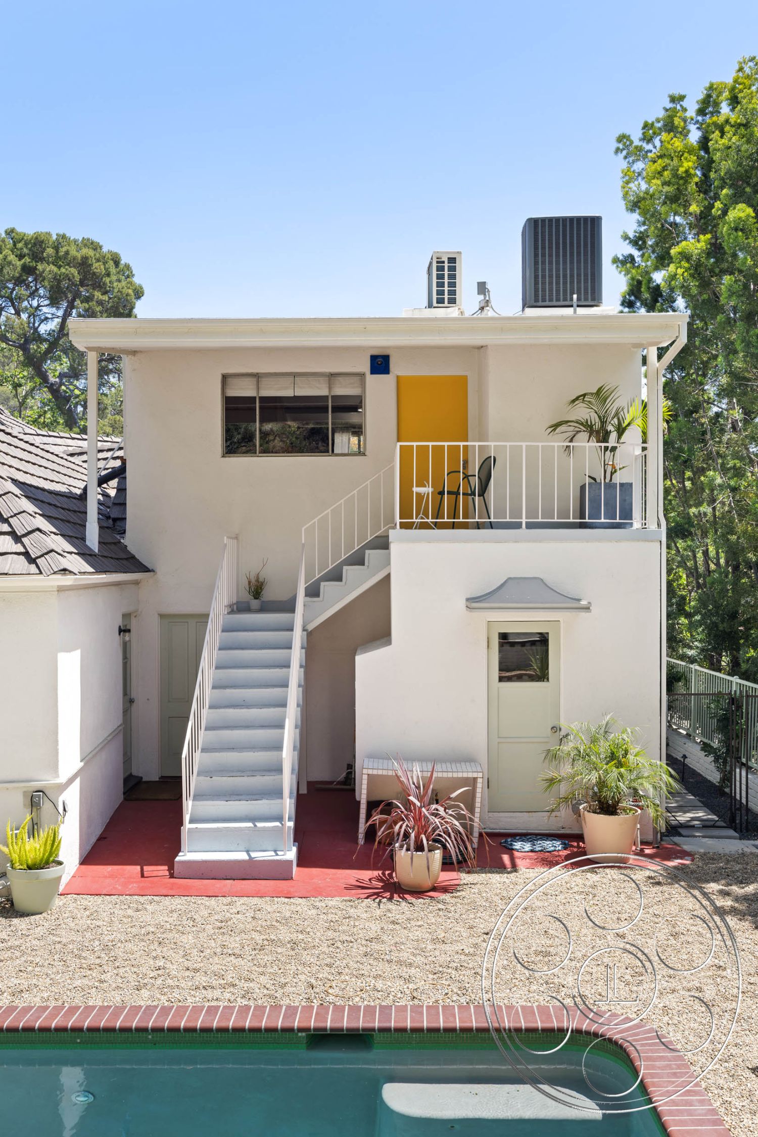 English 60 - white stucco walls, rectangular pool, surrounded by trees, modern residential architecture, exterior concrete patio floor, exterior concrete pool border, interior natural light, exterior gravel landscaping, urban backyard setting, exterior tile pool deck, exterior flat roof, straight staircase, interior outdoor living space, exterior metal railings on stairs, exterior painted wood door, green door feature