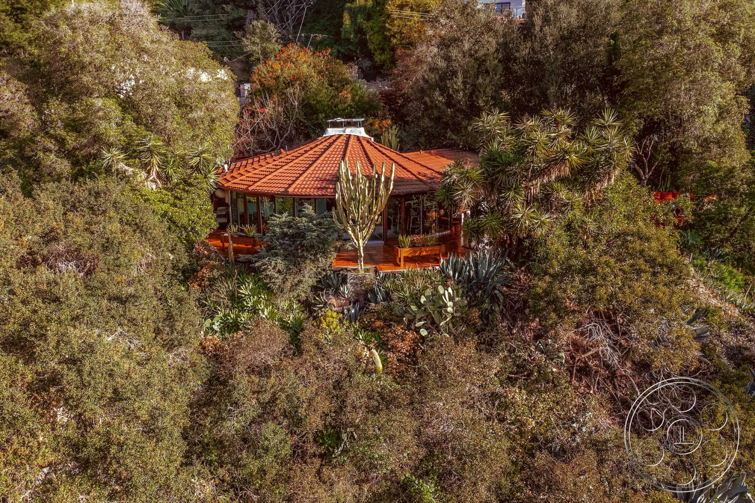 Pad 90210 - exterior, modern design, open floor plan, wooden deck, natural landscaping, floor-to-ceiling windows, red clay tile roof, surrounded by trees, wood beam structure, desert vegetation, urban hillside location, integrated into nature, views of surrounding greenery, circular patio, round house