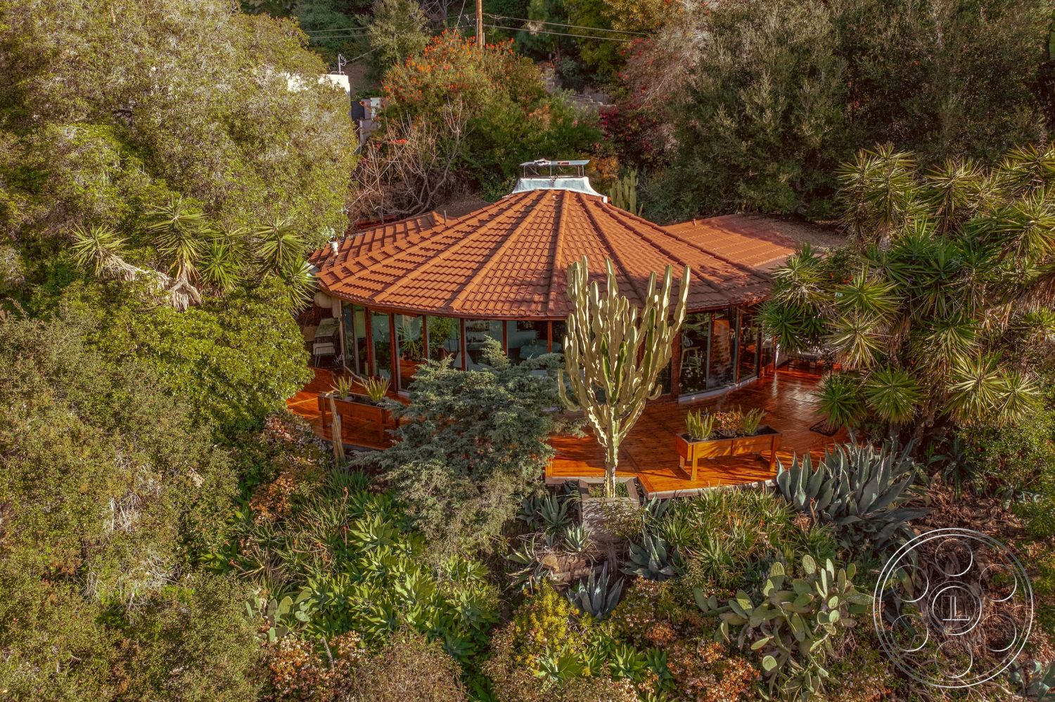 Pad 90210 - floor-to-ceiling windows, modern architectural style, red tile roof, natural wood siding, sun-drenched spaces, sustainable building materials, low-maintenance xeriscaping, open floor plan design, exterior wooden deck, surrounding hillside location, integrated indoor-outdoor living, vaulted ceiling with skylights, circular house shape, surrounding desert landscape, desert flora landscaping, round patio seating area, vibrant greenery surroundings, rustic wooden railings, light airy interior