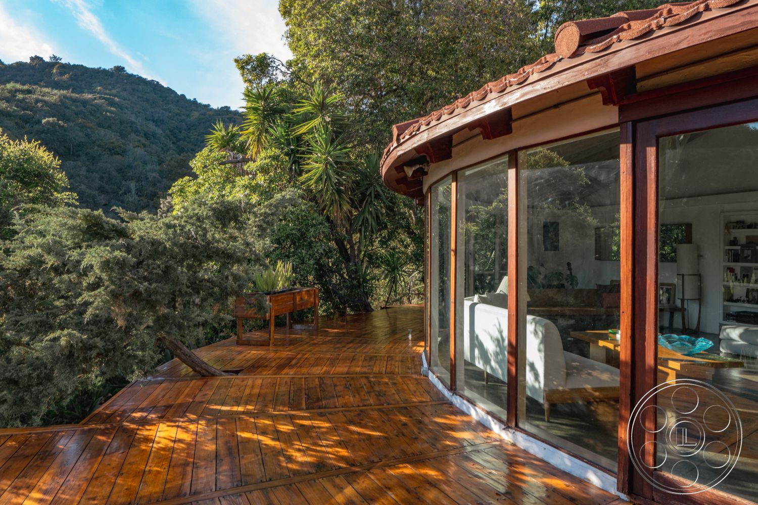 Pad 90210 - natural wood finishes, sustainable architecture, modern organic design, landscaped garden area, exterior wooden deck, open-concept interior, large overhanging eaves, rustic outdoor seating area, curved glass wall, wooden exterior framing, wood beam deck railing, gabled roof with clay tiles, surrounded by forest setting, mountain view patio, terraced wooden flooring