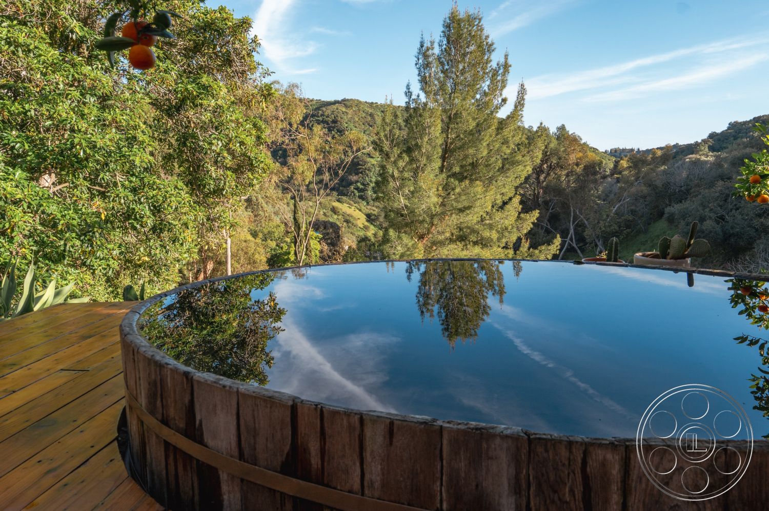 Pad 90210 - outdoor living space, eco-friendly design, surrounded by greenery, hillside location, natural landscape setting, integrated with nature, wood hot tub exterior, circular wooden deck exterior, reflected sky on water surface, botanical environment, serene relaxation area, carpenter wooden craftsmanship