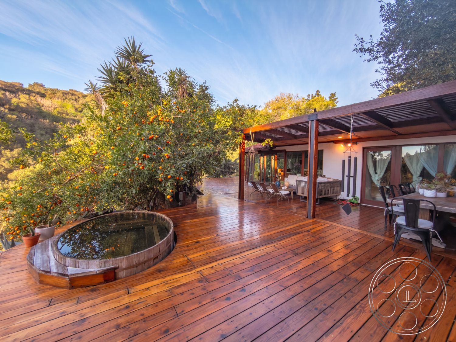Pad 90210 - wooden patio furniture, natural landscape setting, covered outdoor seating area, exterior wooden deck flooring, floor-to-ceiling glass doors, rustic outdoor aesthetic, open outdoor living space, pergola with wooden beams, wood deck with hot tub area, surrounding greenery with citrus trees, hillside location with mountain views, deck with circular seating arrangement