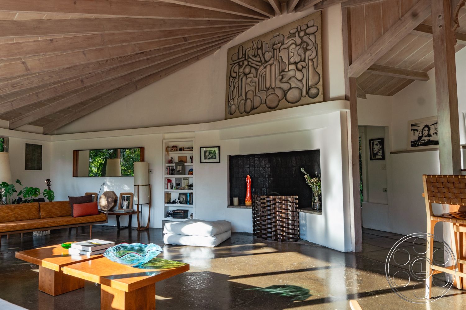 Pad 90210 - interior garden view, exposed wood ceiling beams, minimalist decor accents, modern wooden coffee table, white painted walls, open concept living area, vaulted ceiling interior, contemporary art wall feature, concrete floor with polished finish, dark stone fireplace surround, built-in bookshelf with decorative elements, natural light with large windows, mid-century modern style furnishings, textured wall art installation, wooden lounge chair with woven details