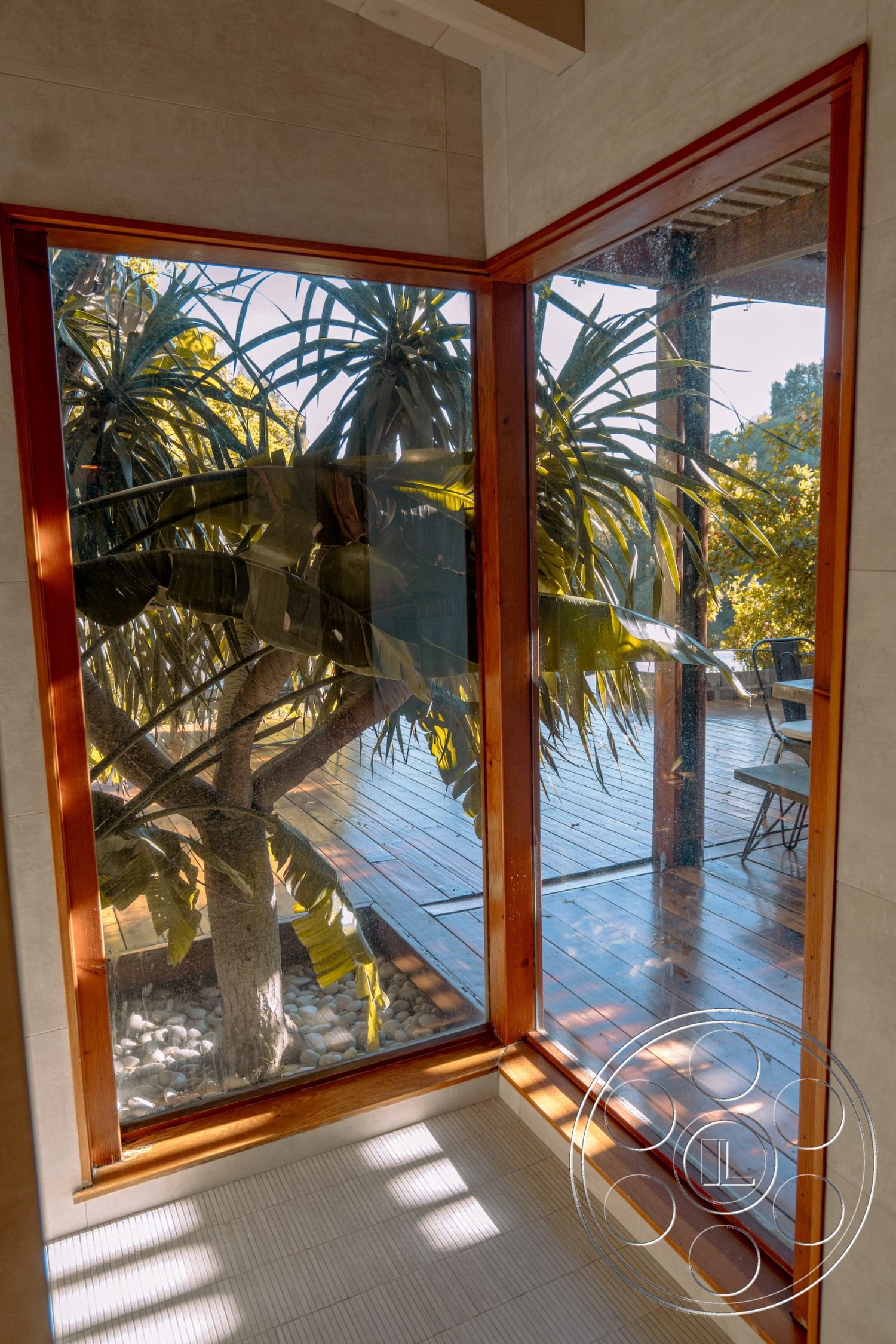 Pad 90210 - exterior shaded outdoor seating area, exterior landscaped garden view, interior natural light from large windows, interior modern architectural design, interior high ceilings, interior seamless indoor-outdoor flow, exterior deck with wooden planks, interior tiled flooring, exterior wooden window frames, interior glass corner windows, interior stone wall accents, exterior tropical plant surroundings, exterior wooden deck support beams, exterior sunlit garden patio, interior minimalist interior aesthetics, exterior views of greenery, interior natural materials usage