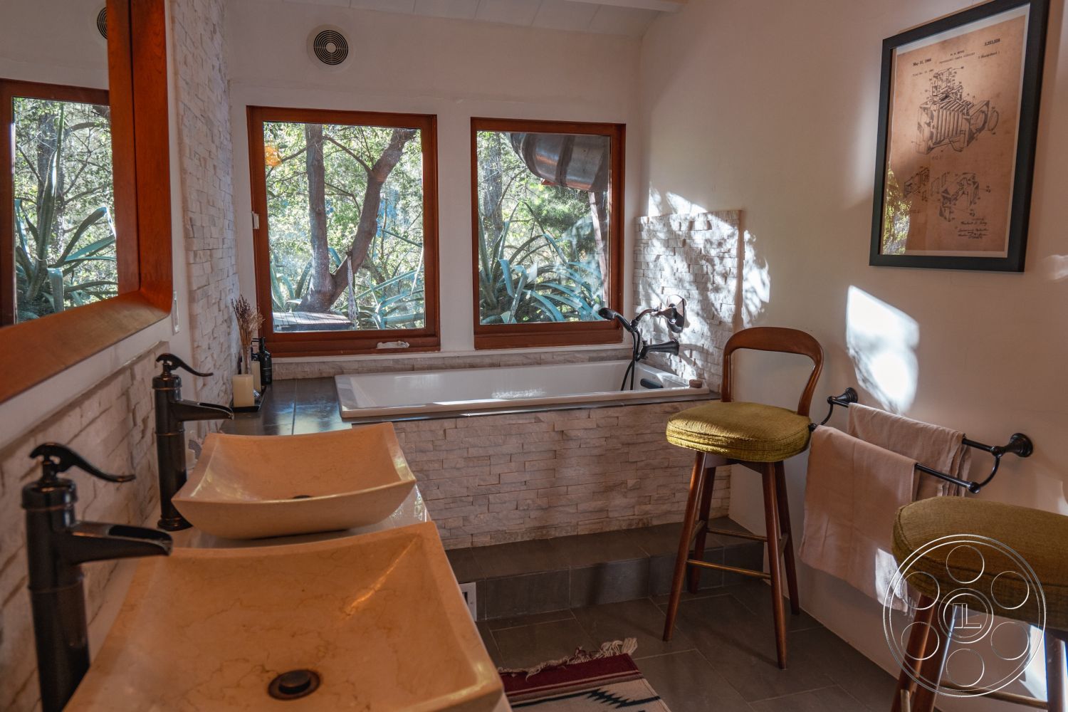 Pad 90210 - dark wood cabinetry, minimalist decor, neutral color palette, natural light, freestanding bathtub, contemporary fixtures, greenery view, stylish bar stools, stone feature wall, warm wood accents, wood-framed windows, hexagonal tile flooring, modern bathroom design, marble countertop sinks, glass vessel sinks, dual vessel sink vanity