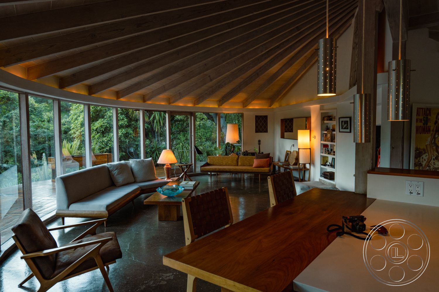 Pad 90210 - exposed wood ceiling beams interior, polished concrete flooring interior, floor-to-ceiling glass windows interior, open floor plan living area interior, warm ambient lighting interior, modern wood furniture interior, rounded wall shapes interior, wooden accent wall interior, retro pendant lighting fixtures interior, circular seating arrangement interior, natural green view exterior, contemporary architectural design exterior