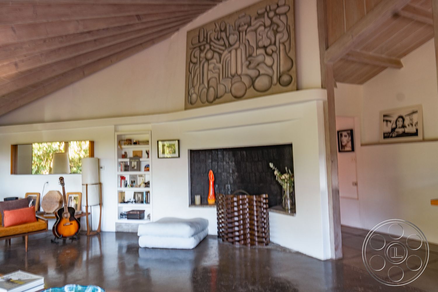 Pad 90210 - neutral color palette, natural light from large windows, open living space, mid-century modern furniture, cozy reading nook, minimalist interior design, wooden furniture accents, interior polished concrete flooring, contemporary art display, built-in wooden bookshelves, rectangular living room layout, spacious entertainment area, sloped wood beam ceiling, exposed concrete fireplace surround, textured concrete wall art, vaulted ceiling design, accent orange decor elements, geometric wall sculpture