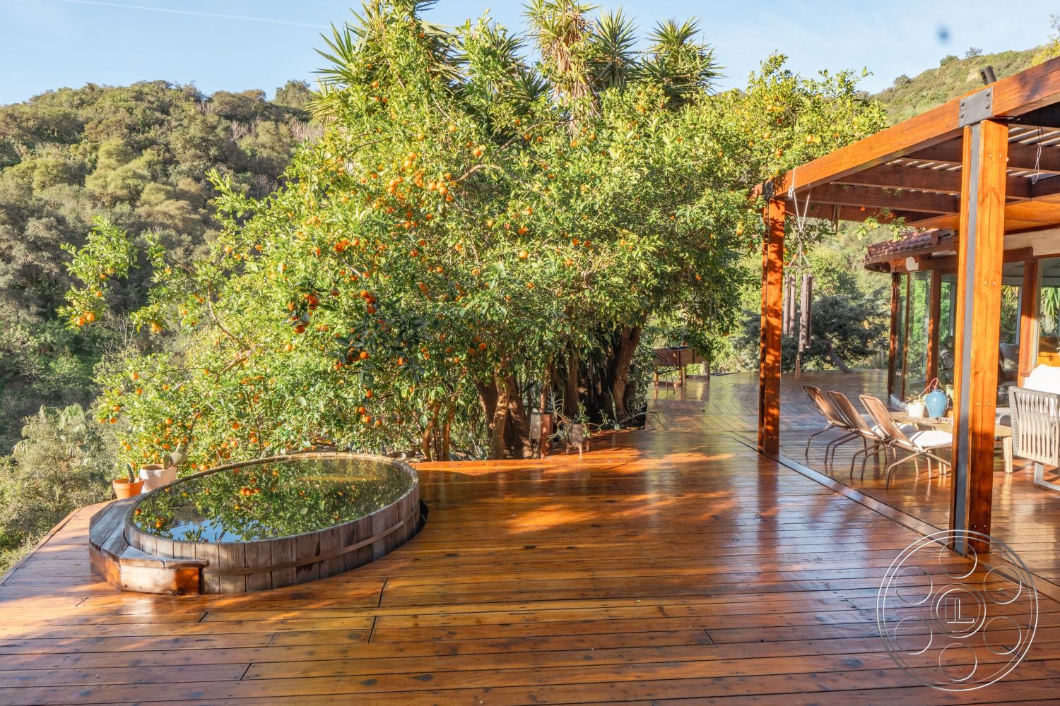Pad 90210 - large glass windows, contemporary outdoor space, modern outdoor seating, exterior wood deck flooring, round wooden hot tub, surrounding natural hillside setting, deep green foliage, open-air patio area, rustic wooden beam structure