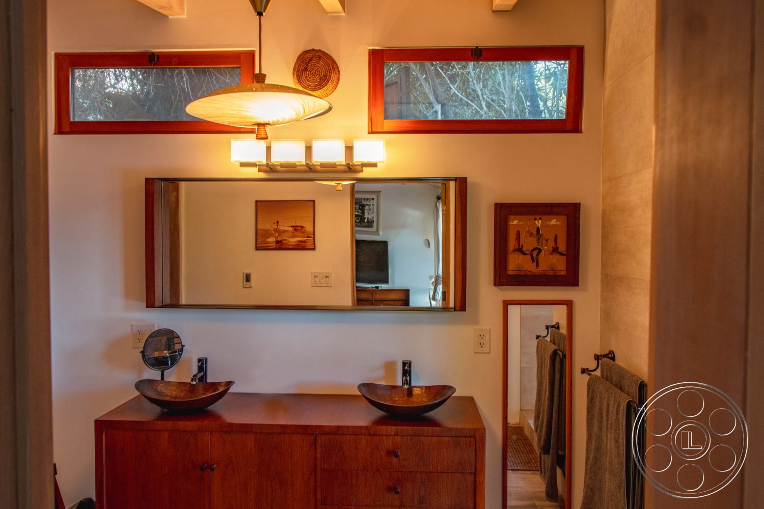 Pad 90210 - exposed beam ceiling, neutral painted walls, framed artwork wall decor, wood vanity cabinet with sink basins, medium brown hardwood bathroom flooring, glass wall bathroom mirror, ambient light pendant fixture, large window with red trim, towel rail fixtures, minimalist contemporary bathroom design, interior ambiance with natural light