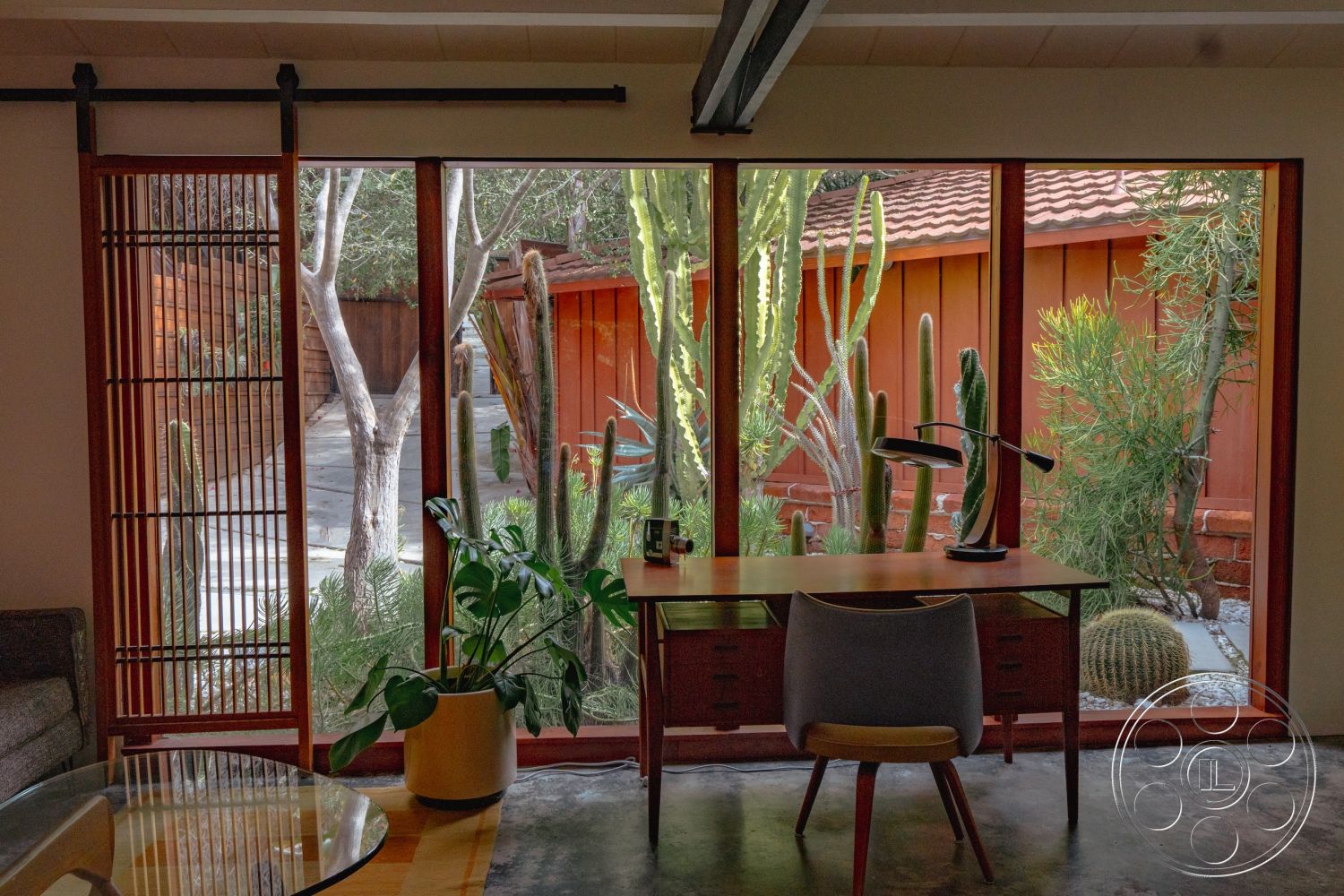 Pad 90210 - neutral color palette, concrete floor, cozy reading nook, mid-century modern style, contemporary art piece, natural light setting, wood beam ceiling, decorative indoor plants, modern desk lamp, minimalist desk design, exposed wooden furniture, interior wooden sliding door, interior glass window walls, cactus garden view, slatted wood partition, wooden wall siding, stone landscape details, open indoor space