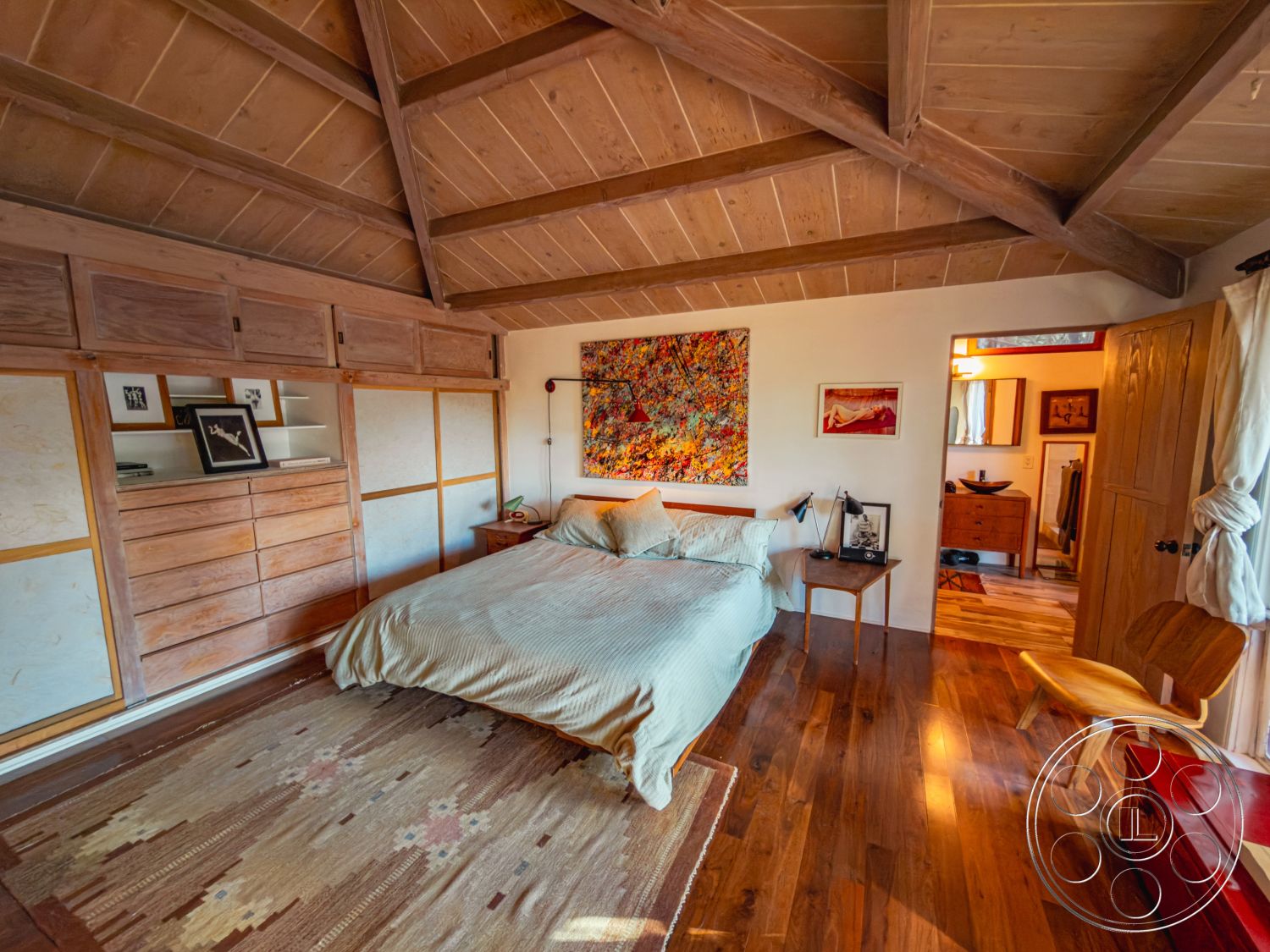 Pad 90210 - colorful wall art, warm ambient lighting, cozy reading nook, modern bedside lamps, exposed wood ceiling beams, natural light through window, hardwood bedroom floors, interior bedroom setting, textured white walls, built-in wood storage cabinets, carpet area rug, wooden doorframe, simple yet elegant decor