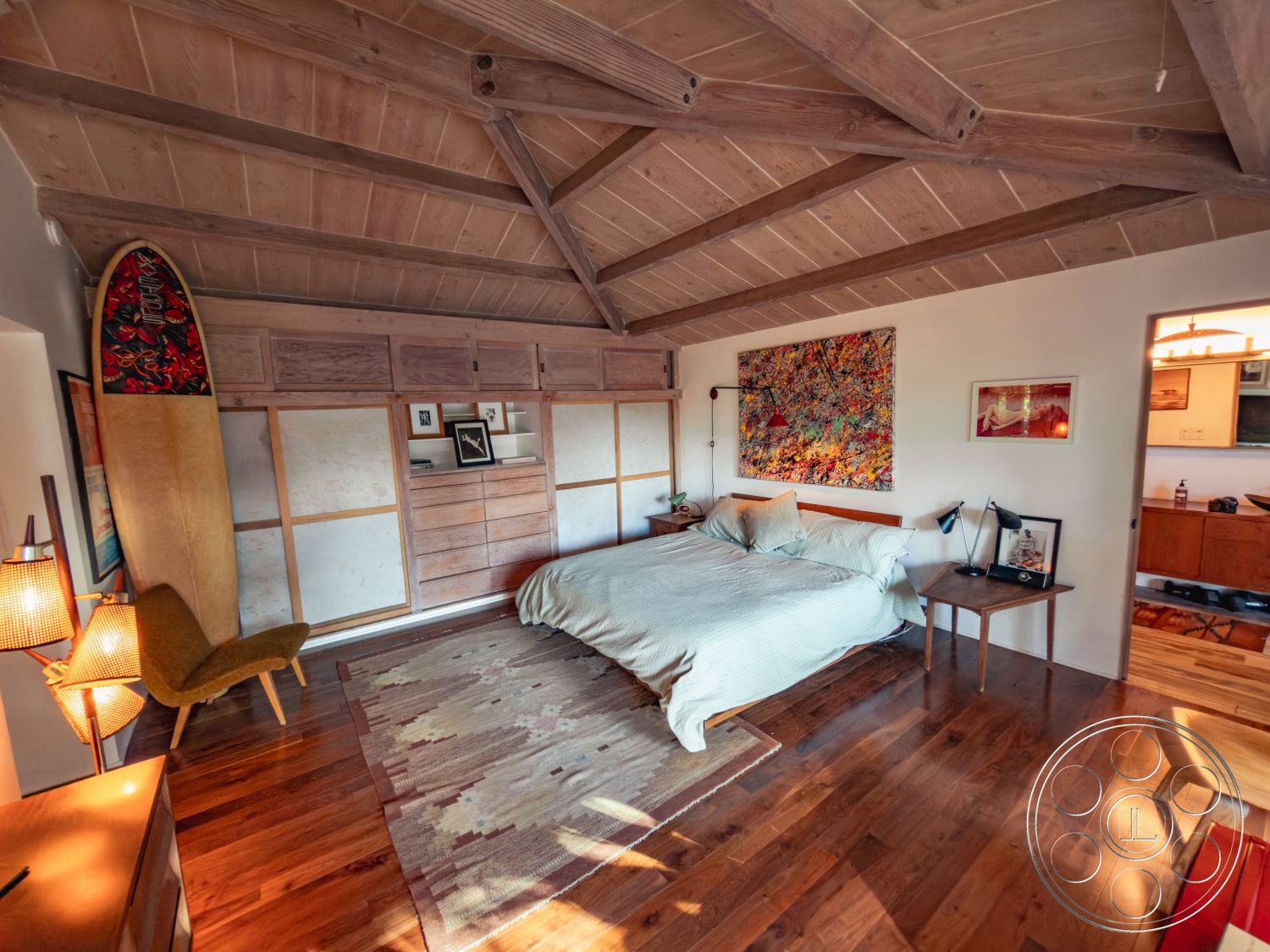 Pad 90210 - warm wood tones, relaxing atmosphere, textured wall finishes, plush area rug, mid-century modern style, efficient space utilization, open-plan layout, exposed wood ceiling beams, hardwood bedroom floors, white painted walls, modern artwork wall decor, modern furniture design, natural light flooding interior, built-in wood cabinetry, contemporary bedside lamps, cozy bedroom nook, surfboard decoration