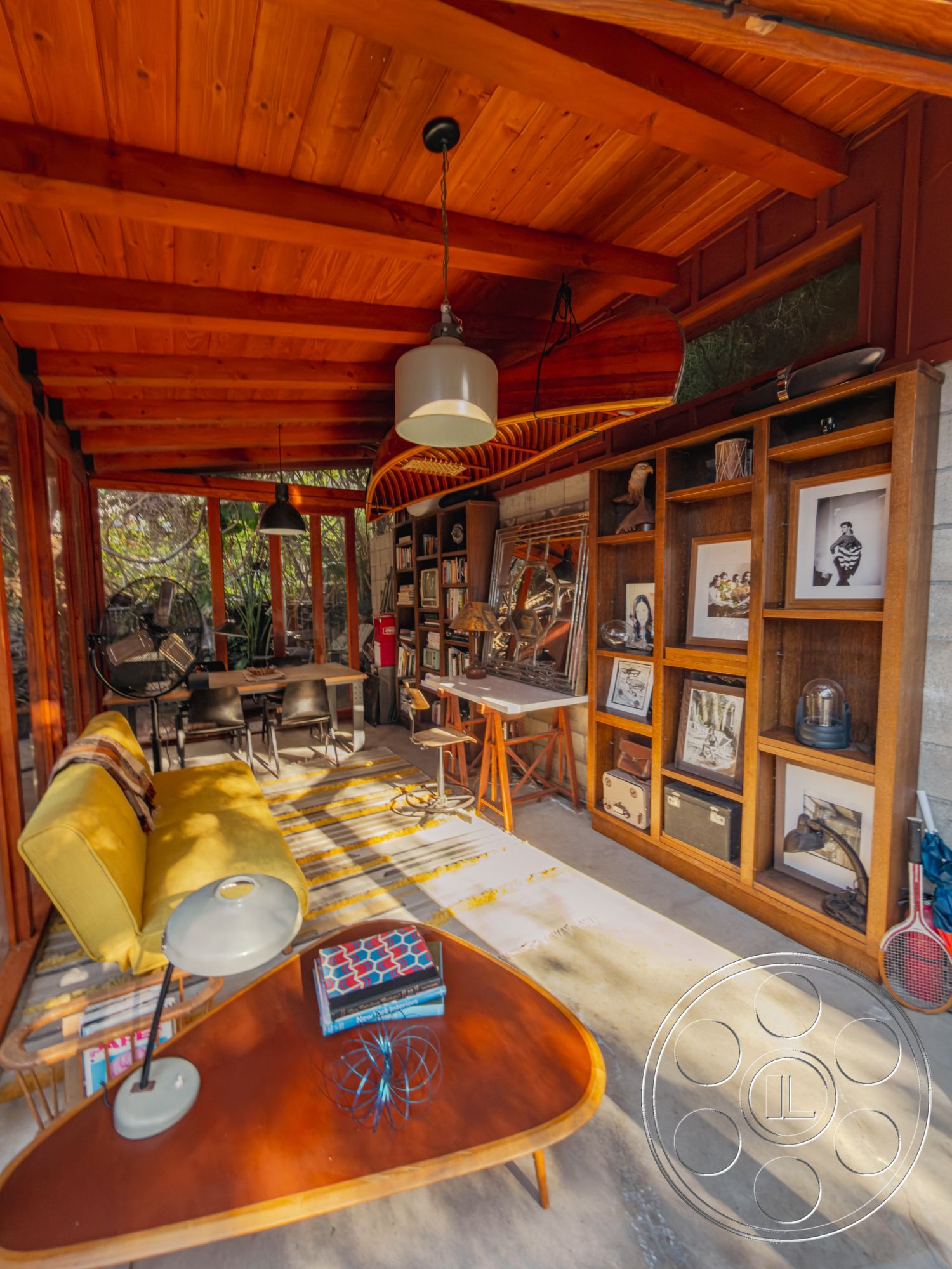 Pad 90210 - concrete floor, minimalist coffee table, cozy reading nook, modern lounge area, wooden shelving unit, mid-century modern style, industrial light fixtures, wood beam ceiling, contemporary workspace, exposed wood paneling, indoor garden view, yellow velvet sofa, natural light from large openings, glass interior doors, decorative art displays, rugged textile accents, open-air interior space