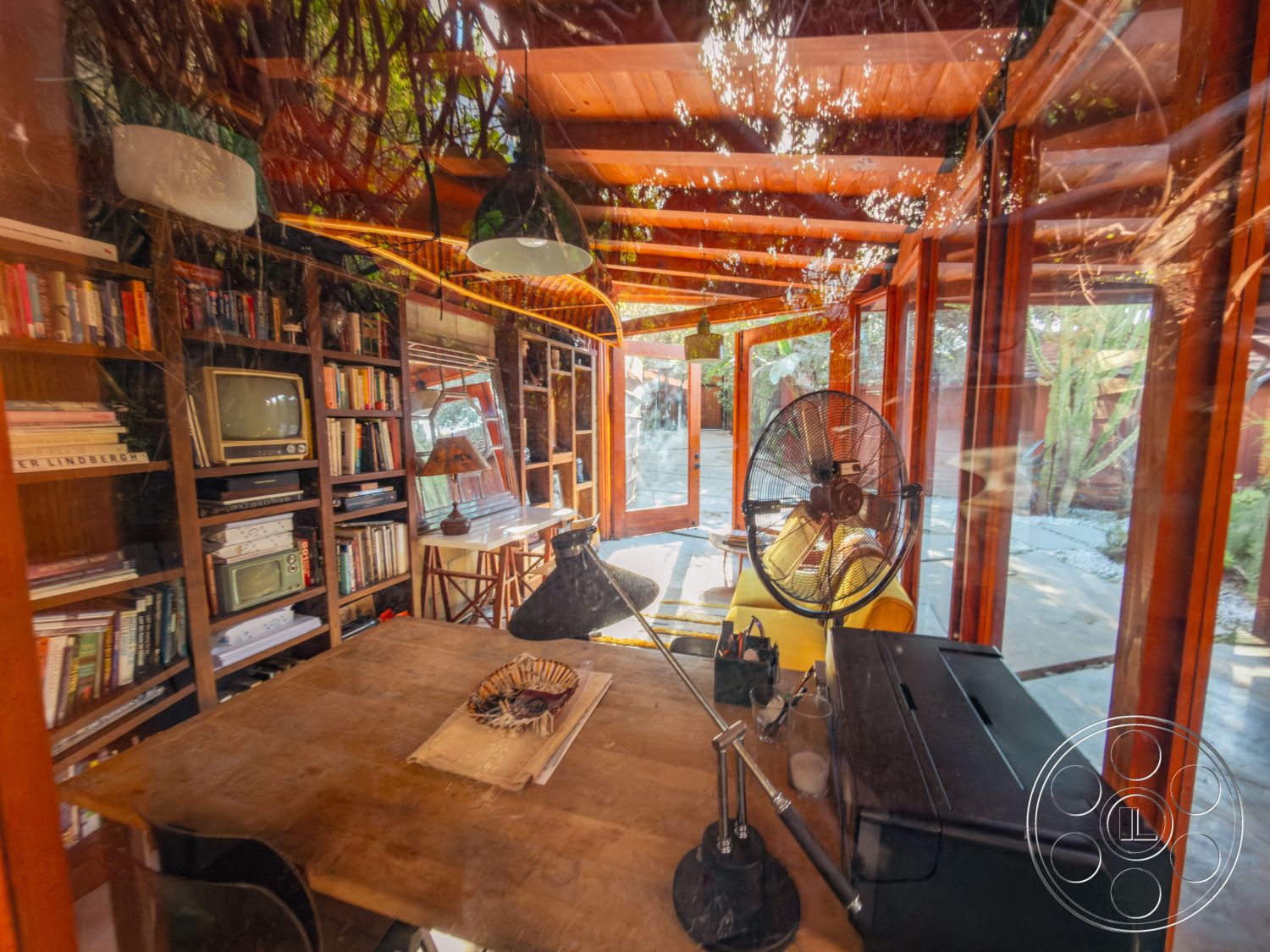 Pad 90210 - wooden flooring, open floor plan, textured wall finish, bright natural lighting, built-in bookshelf, mid-century modern decor, cozy reading nook, rustic wooden dining table, indoor plant accents, glass wall panels, interior wooden ceiling beams, modern pendant light fixtures, exposed wood frame structure, vintage television display, stylish black table lamp, intimate dining area