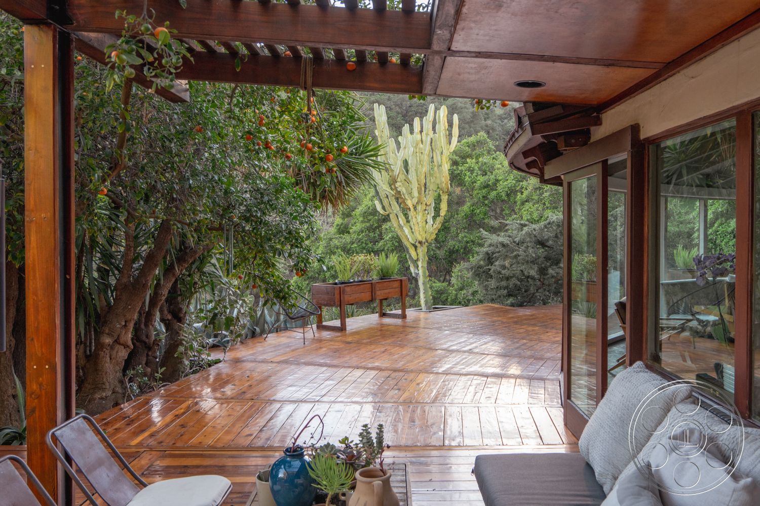 Pad 90210 - outdoor seating area, natural wood furniture, lush greenery backdrop, multi-level landscaping, wood beam ceiling, urban garden setting, exterior wooden deck flooring, floor-to-ceiling glass panels, wooden pergola structure, surrounding tropical landscape, exposed timber elements, patio with built-in seating, rustic bench seating, open deck design, modern patio decor