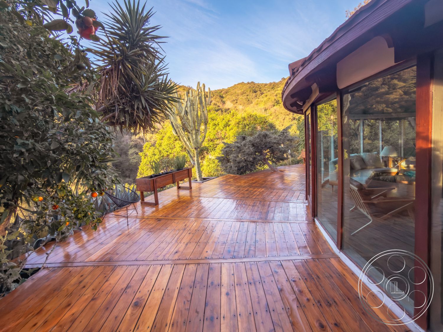 Pad 90210 - outdoor seating area, natural landscaping, open-air living space, mountain view setting, exterior wooden deck flooring, curved exterior walls, rustic outdoor aesthetic, surrounding tropical vegetation, glass sliding door access, rounded wooden deck surface, smooth wood railing, integrated natural environment, pergola-style roof details