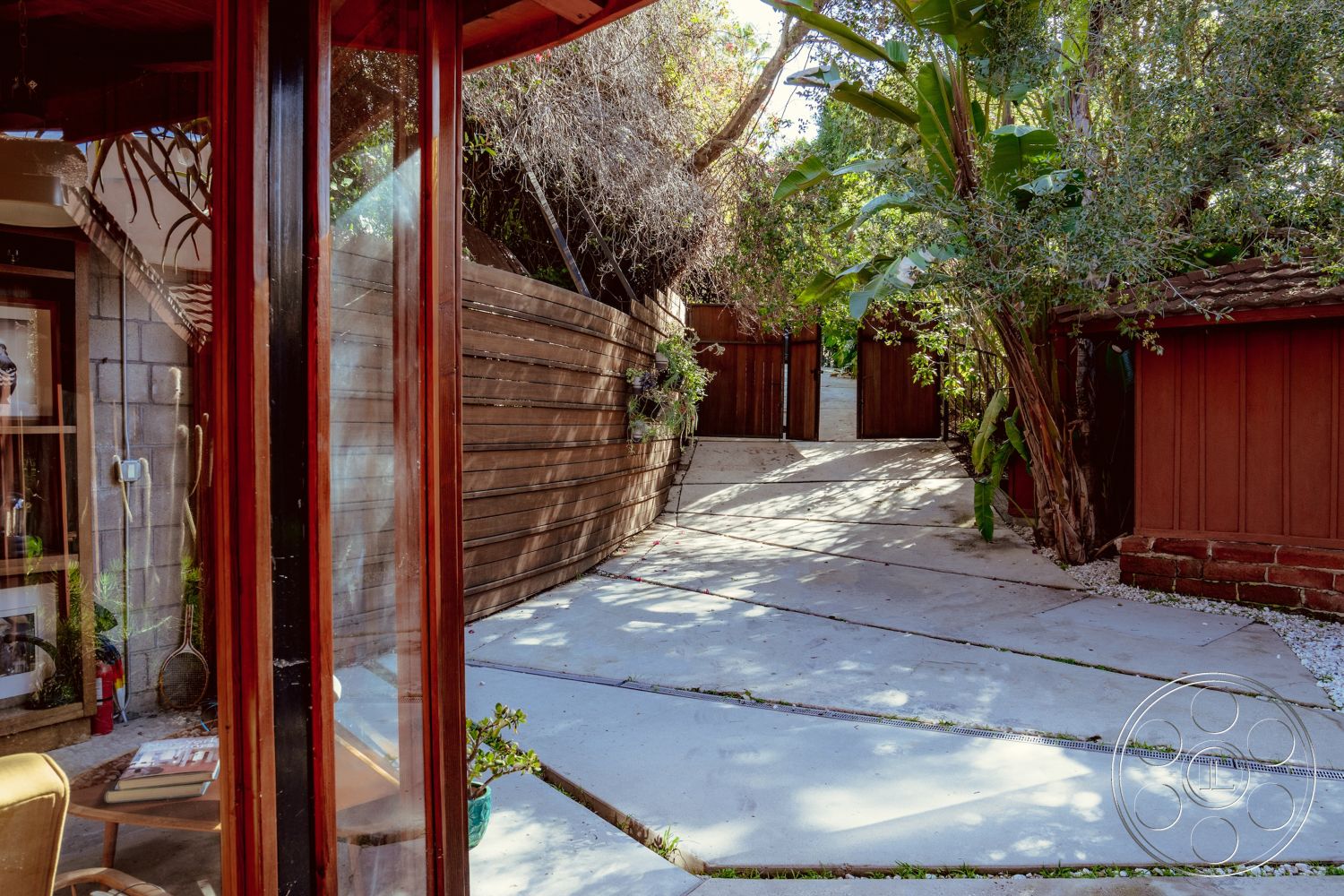 Pad 90210 - outdoor seating area, exterior concrete driveway, modern architectural design, tropical plant landscaping, exposed aggregate concrete surface, landscaped tropical garden, curved concrete walkway, wood fence paneling, redwood garden walls, corrugated metal accents, sloped drive approach, minimalist entrance feature, wooden double gates, contemporary exterior aesthetics, greenery surrounding the property