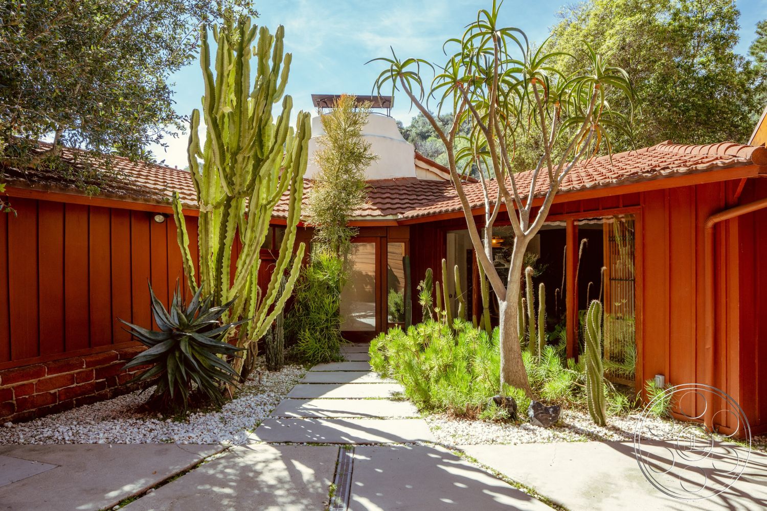 Pad 90210 - exterior, natural stone accents, desert landscaping, clay tile roof, minimalist outdoor design, glass entry doors, mediterranean architectural style, exposed wood structure, single-story layout, sunny courtyard setting, redwood siding walls, slate pathway tiles, succulent plants garden, desert ornamental cacti, white gravel ground cover, arched entrance doorway