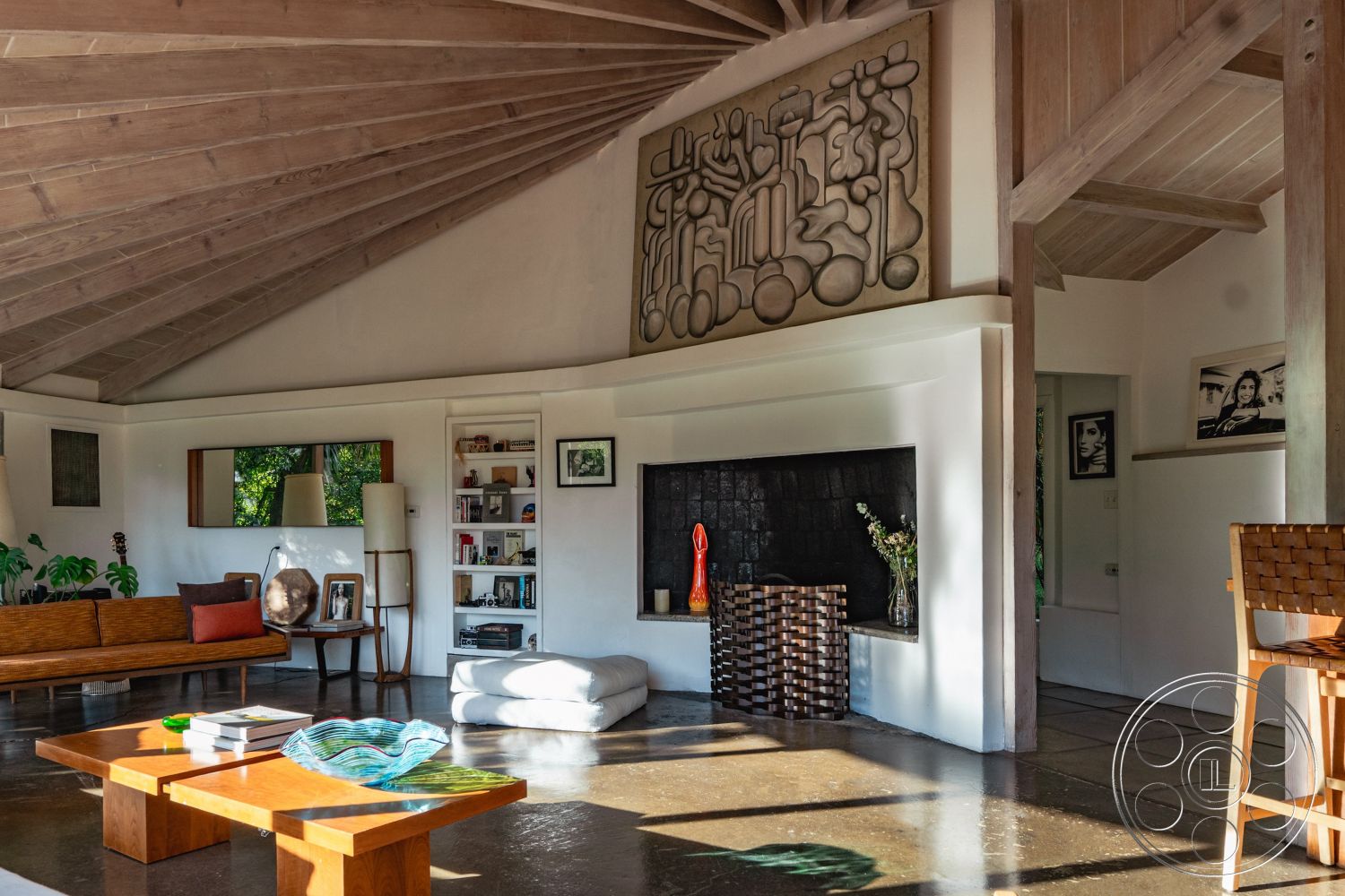 Pad 90210 - neutral color palette, dark wood accents, natural light from large windows, textured plaster walls, open living space, rectangular coffee table, built-in bookshelves, mid-century modern architectural style, exposed brick fireplace surround, minimalist interior design, modern accent decor, interior wood beam ceiling, potted indoor plants, interior polished concrete flooring, modern lounge seating, artistic wall sculpture