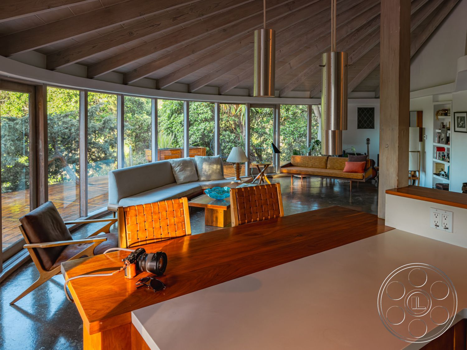 Pad 90210 - interior modern pendant lighting, interior minimalist decor, interior open concept living area, interior cozy seating arrangement, interior natural light-filled space, interior ambient lighting, interior polished concrete flooring, interior hardwood ceiling beams, interior mid-century modern furniture, interior round glass windows, interior wooden dining table, interior woven leather chair, interior wood-paneled walls, interior circular architecture, interior plant-filled environment, interior cohesive color palette